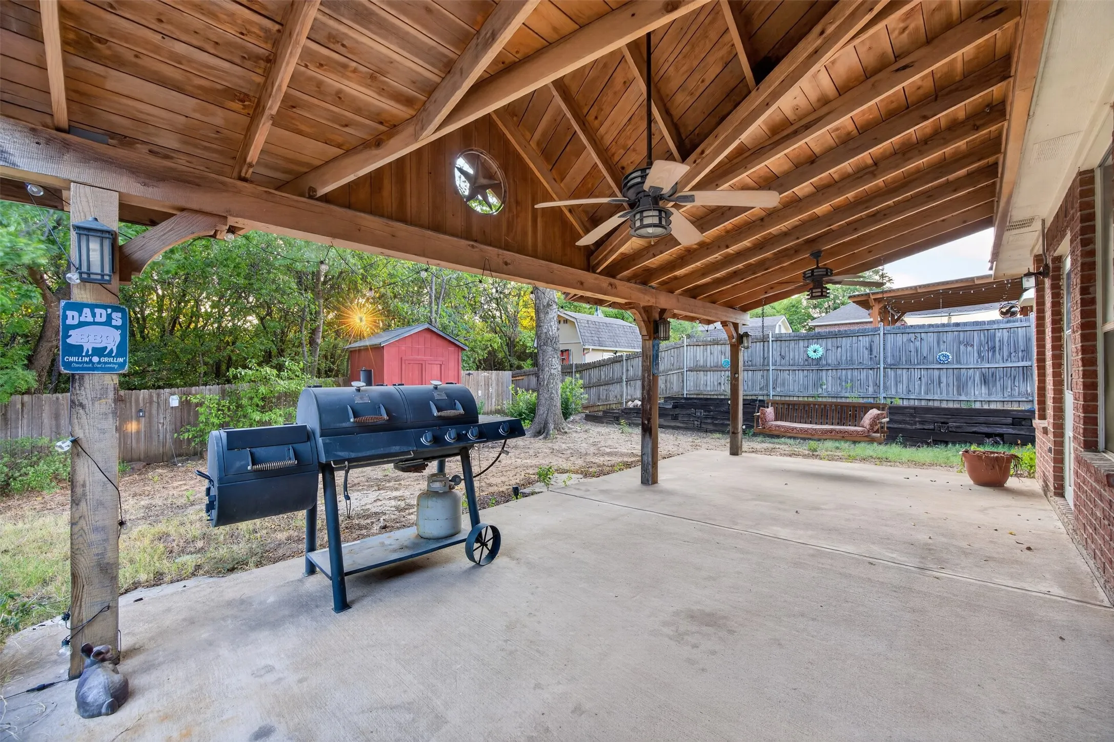 Expansive covered patio with a vaulted wood plank ceiling, two ceiling fans, and concrete flooring