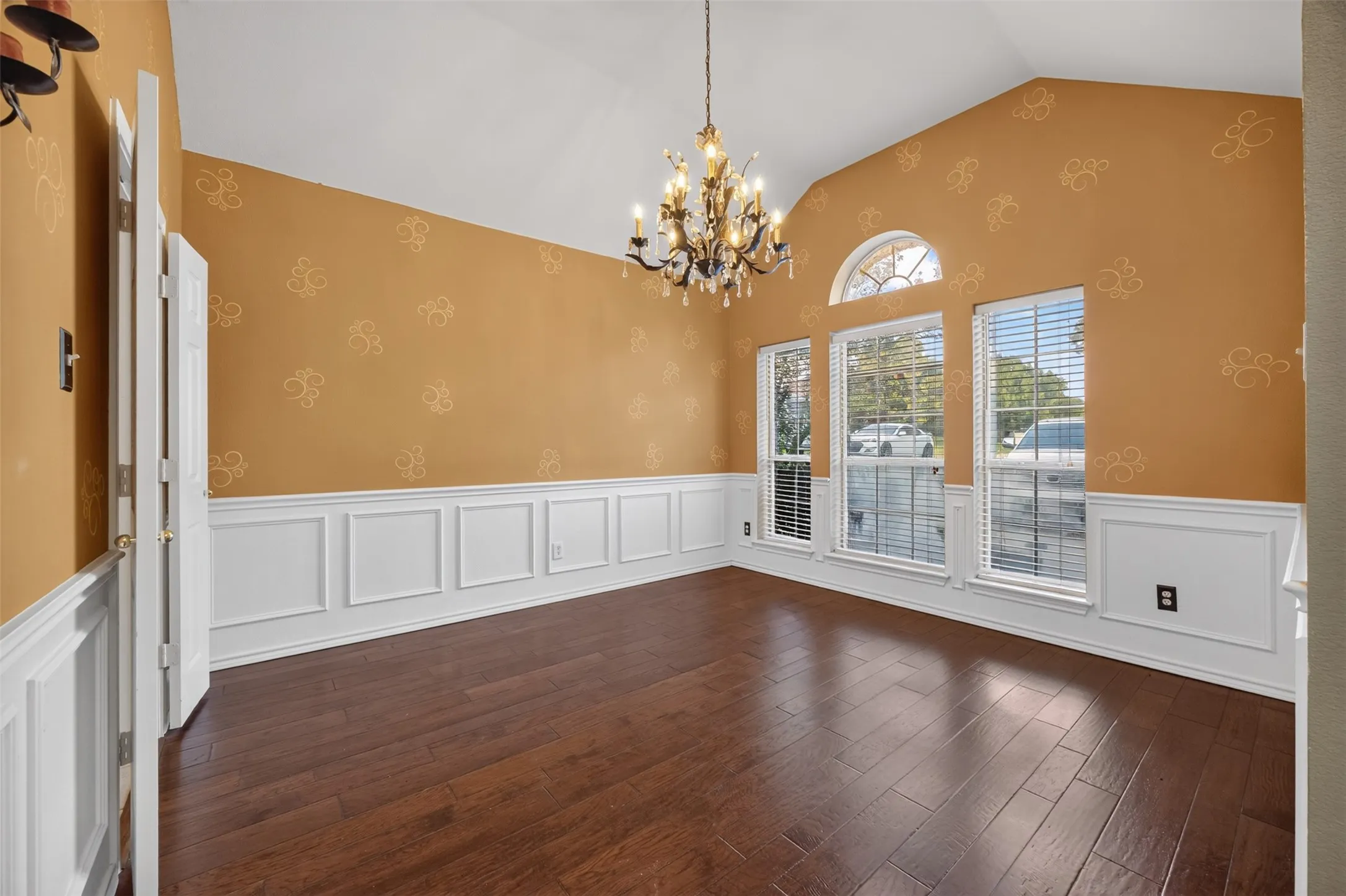 Vaulted ceiling with an ornate chandelier, wood-finish flooring, wainscoting, and large windows with an arched transom