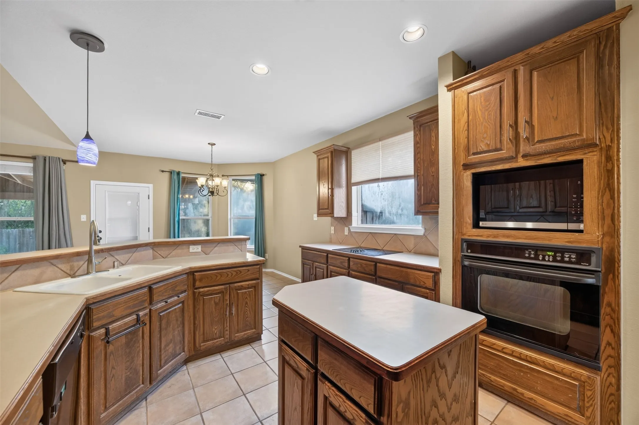 Kitchen featuring wood cabinetry, built-in microwave and oven, a central island, and a dual-basin sink