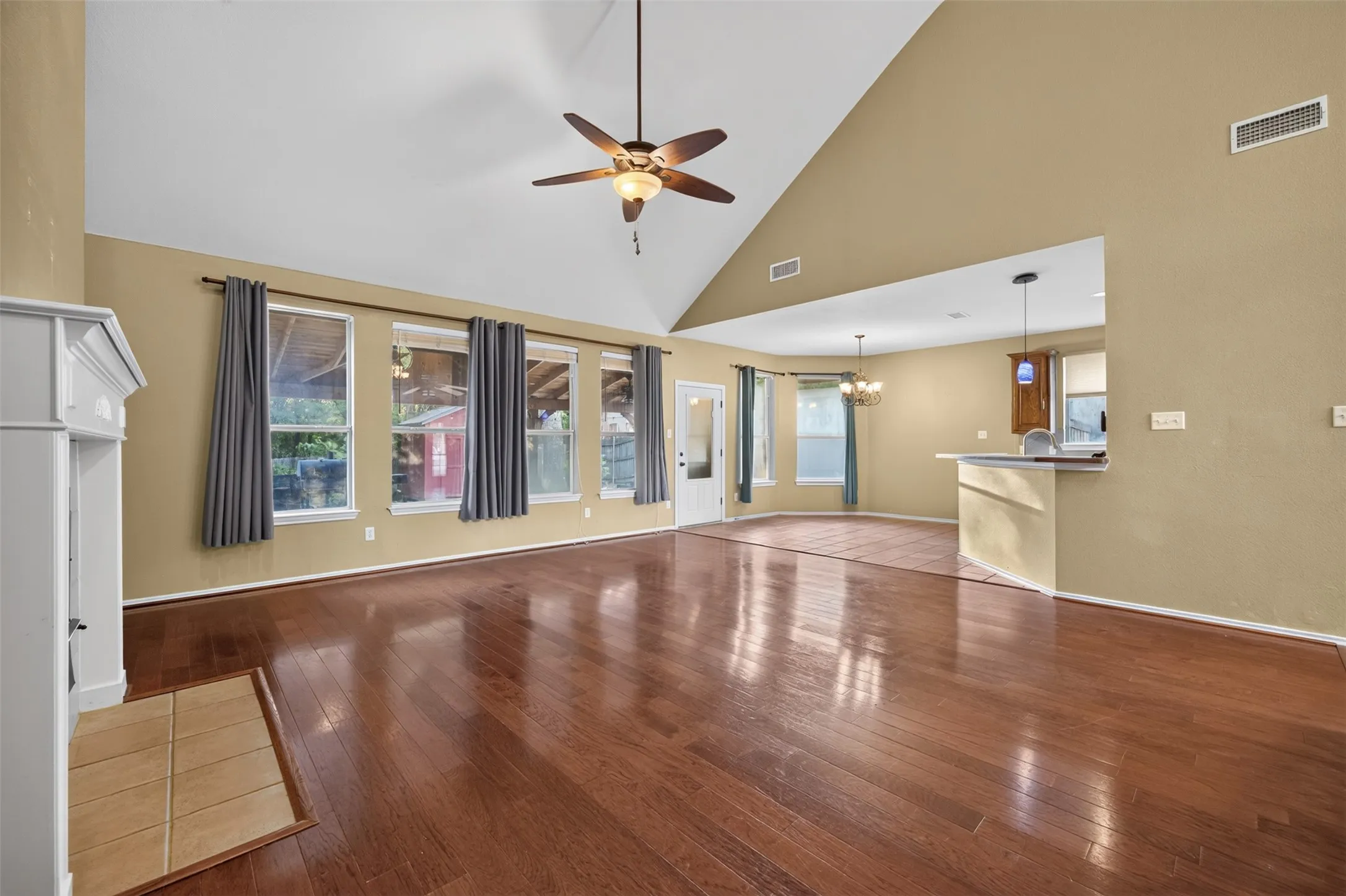 Vaulted ceiling with a ceiling fan, wood-finish flooring, fireplace with tile hearth, multiple windows, and a breakfast bar