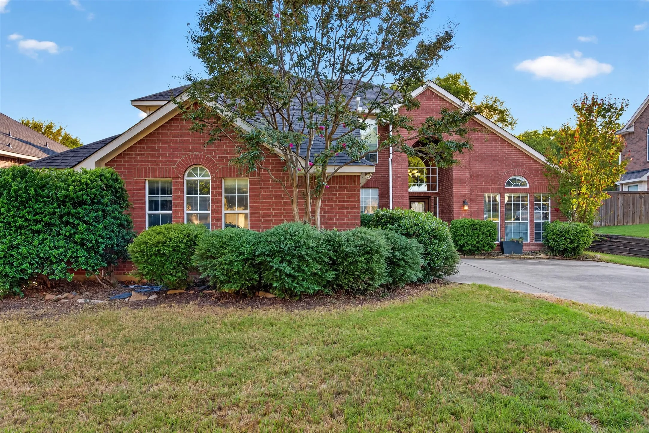 Red brick exterior with arched windows, mature landscaping, and a concrete driveway