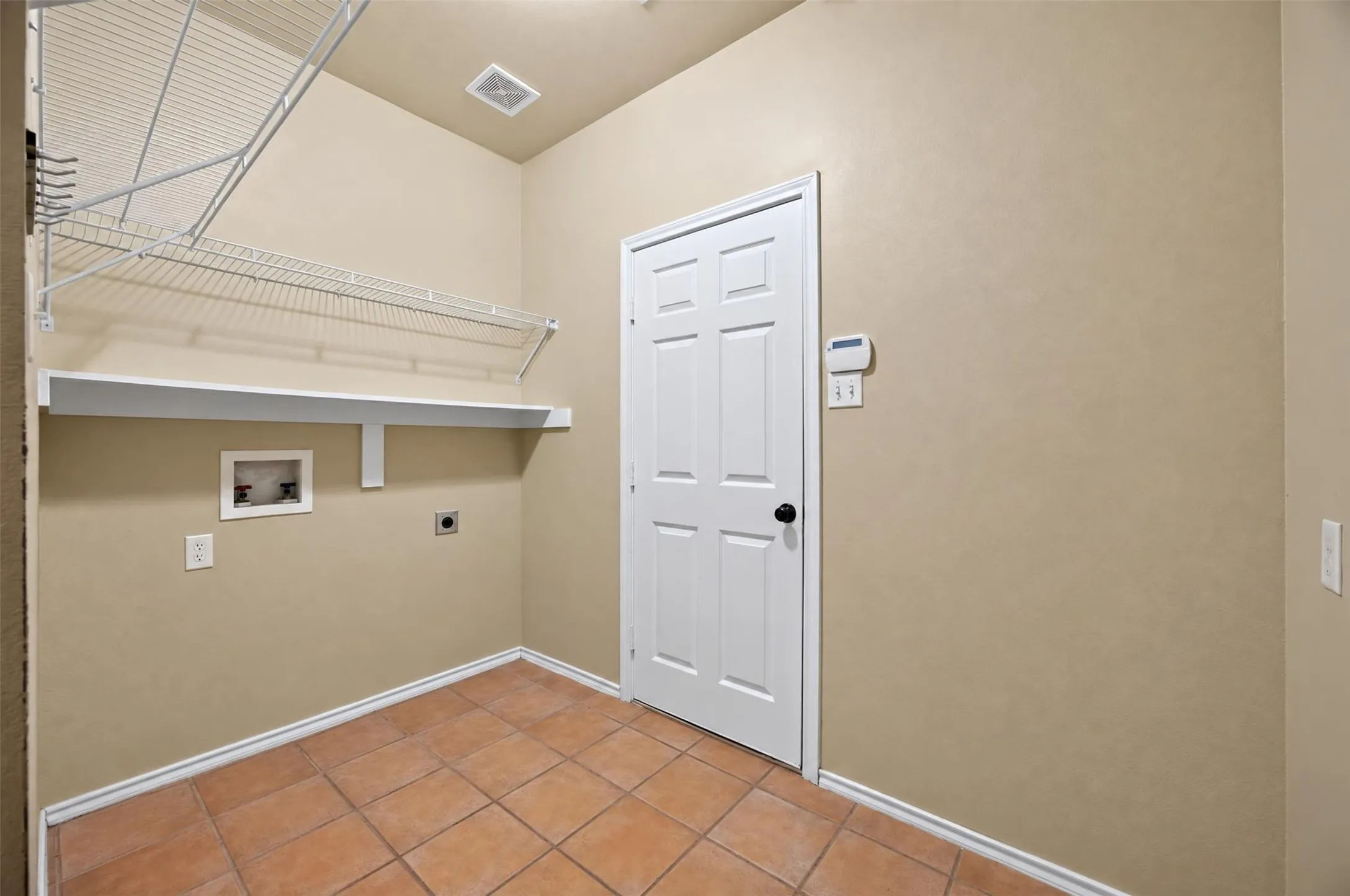 Laundry area featuring terracotta-style tile flooring, built-in wire shelving, and a wall-mounted utility shelf