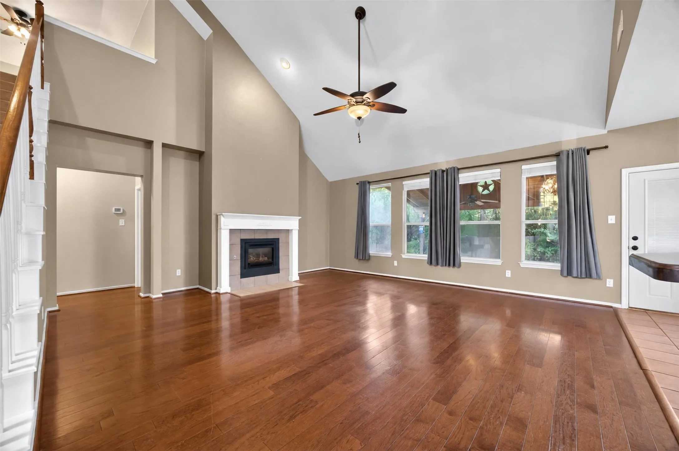 Vaulted ceiling with a ceiling fan, wood-finish flooring, fireplace with a tile surround and white mantel, multiple windows, and a white door with a window