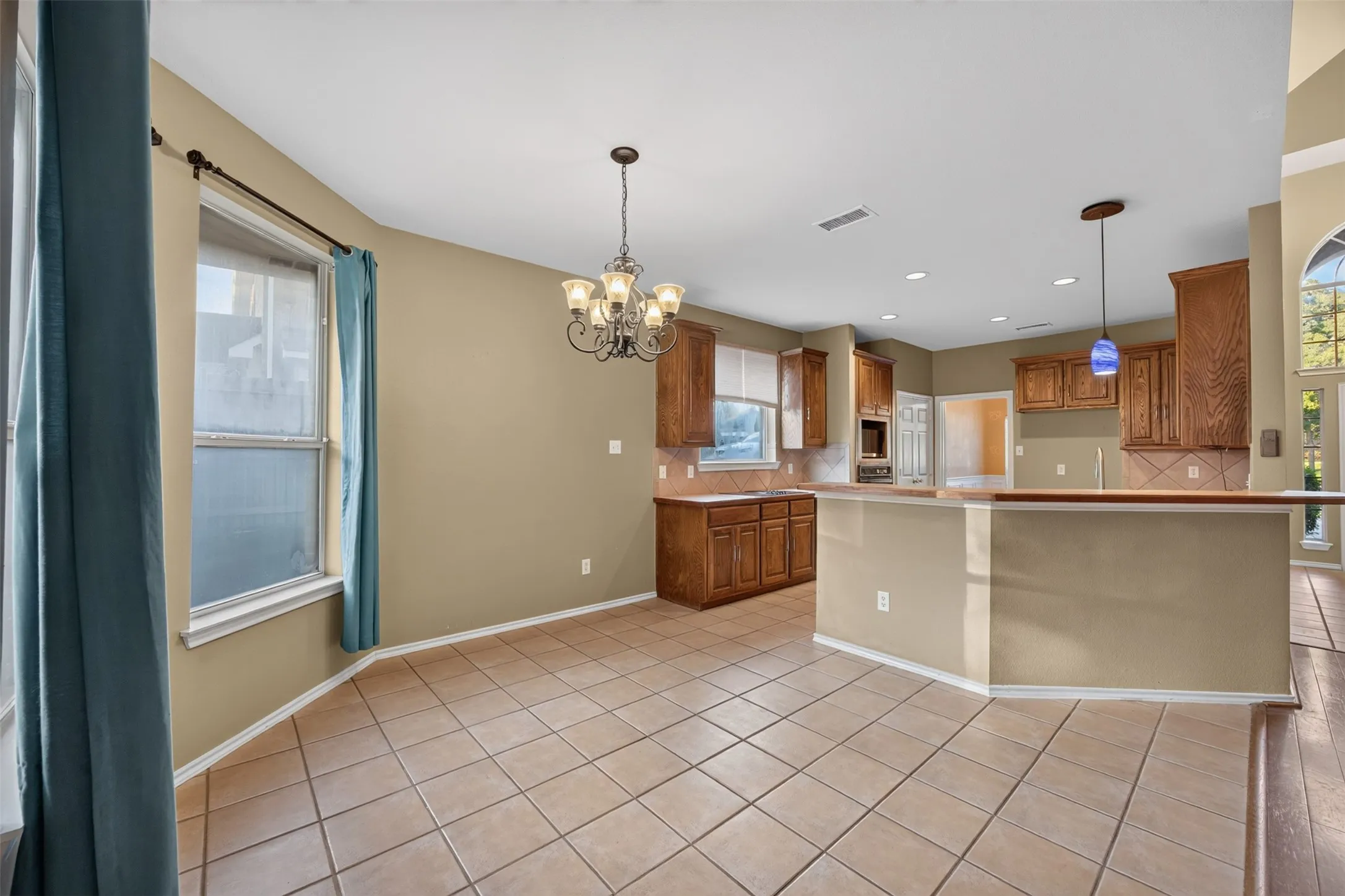 Open-concept kitchen and dining area featuring tile flooring, wood cabinetry, built-in appliances, and a breakfast bar