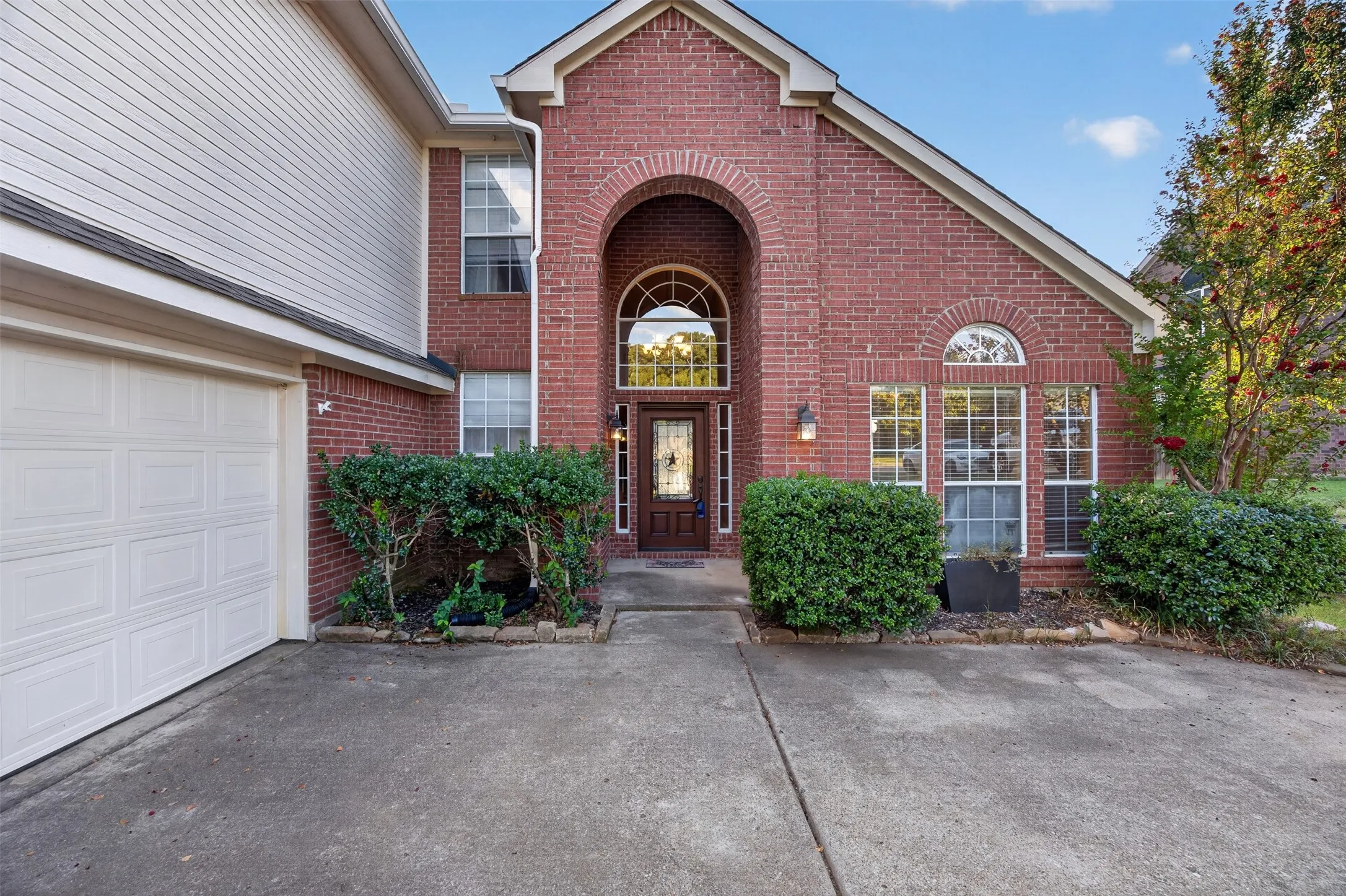Brick facade with arched entryway, decorative transom window, and a paneled garage door