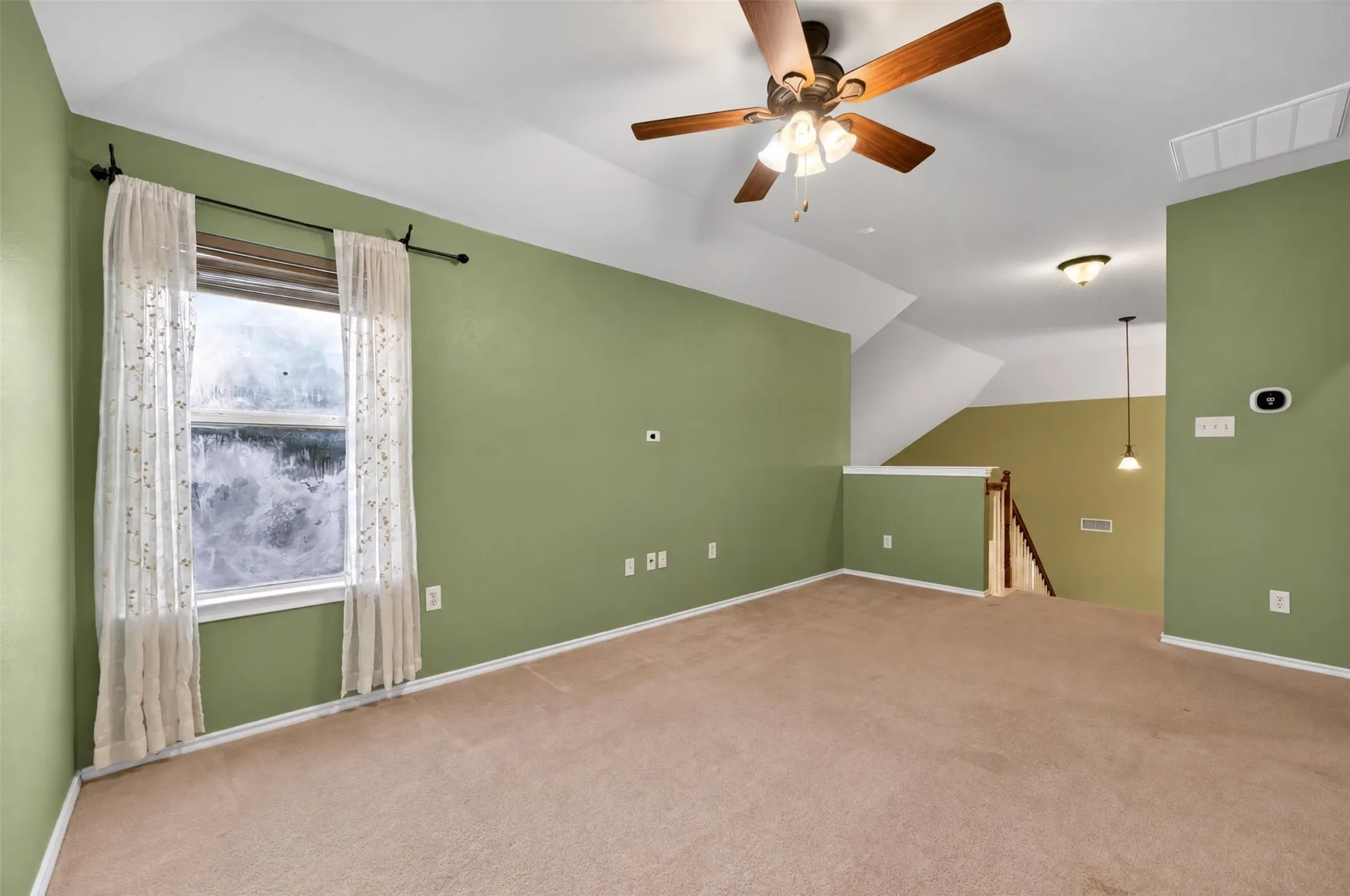 Spacious room with sloped ceilings, a ceiling fan, and carpeted flooring