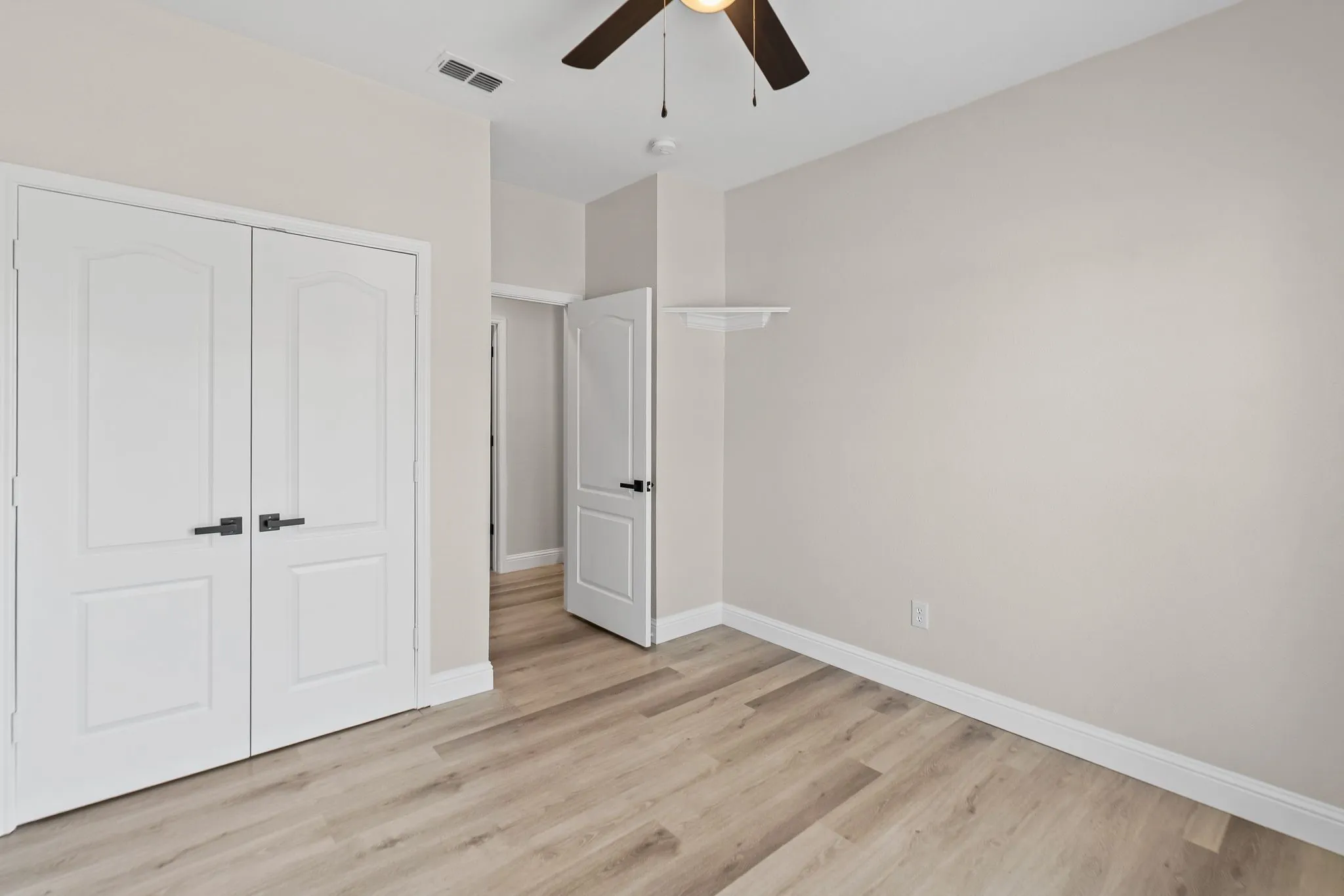 Third bedroom, with wood-finish flooring, white paneled doors with dark hardware, ceiling fan with light fixture, light-toned walls, and white trim