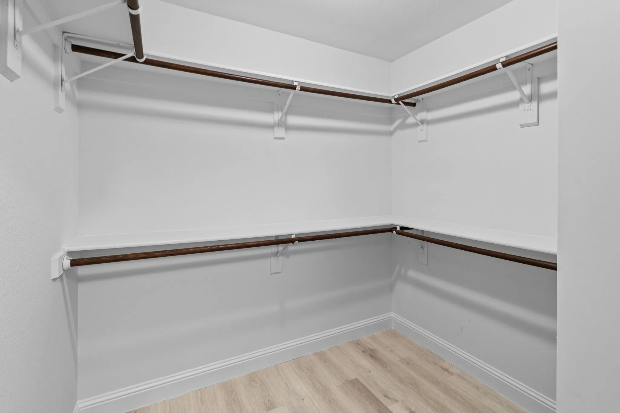 Walk-in closet with multiple hanging rods, white shelving, and wood-finish flooring