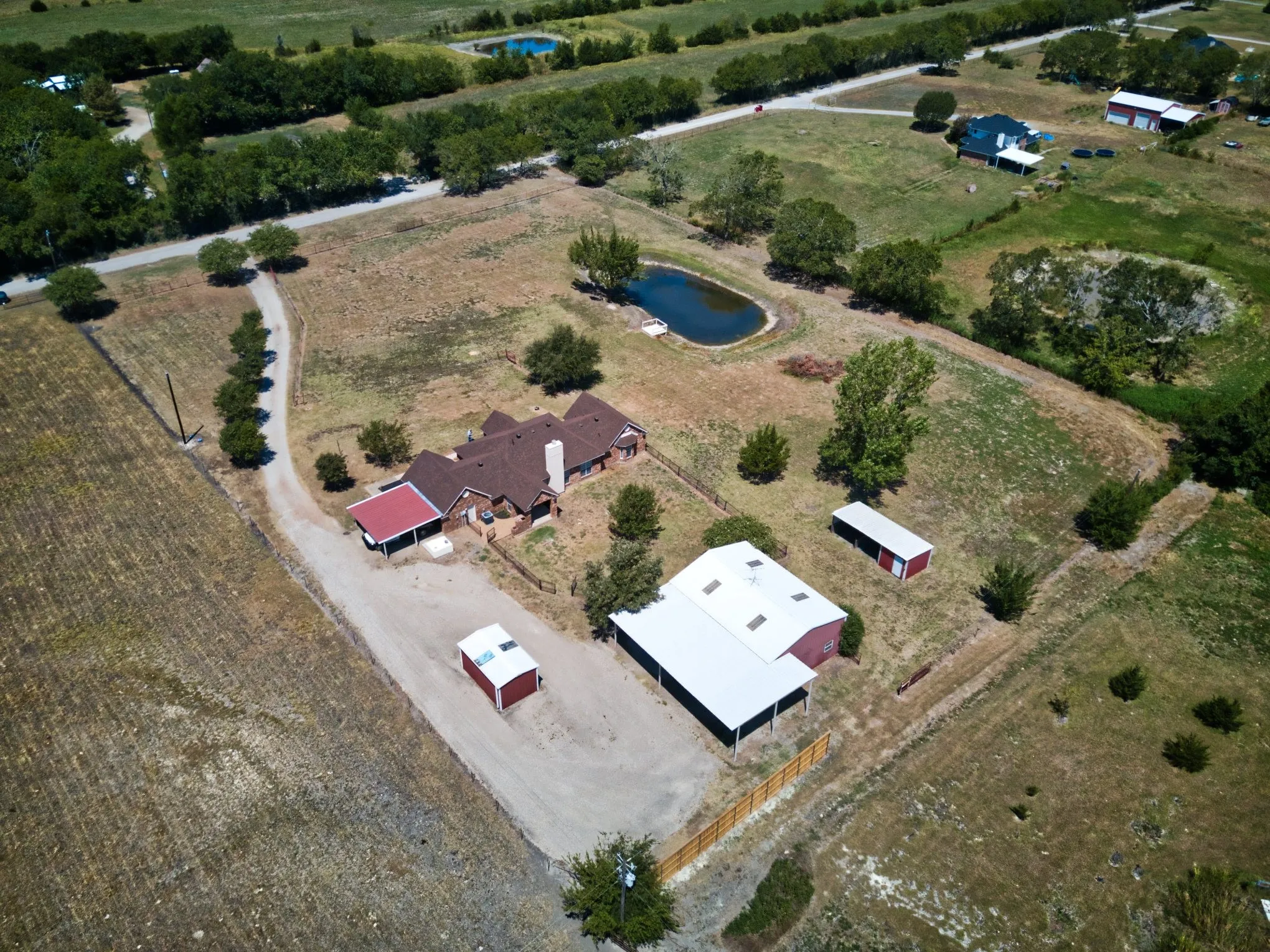 Expansive property featuring a main residence, detached outbuildings, a pond, and a gravel driveway