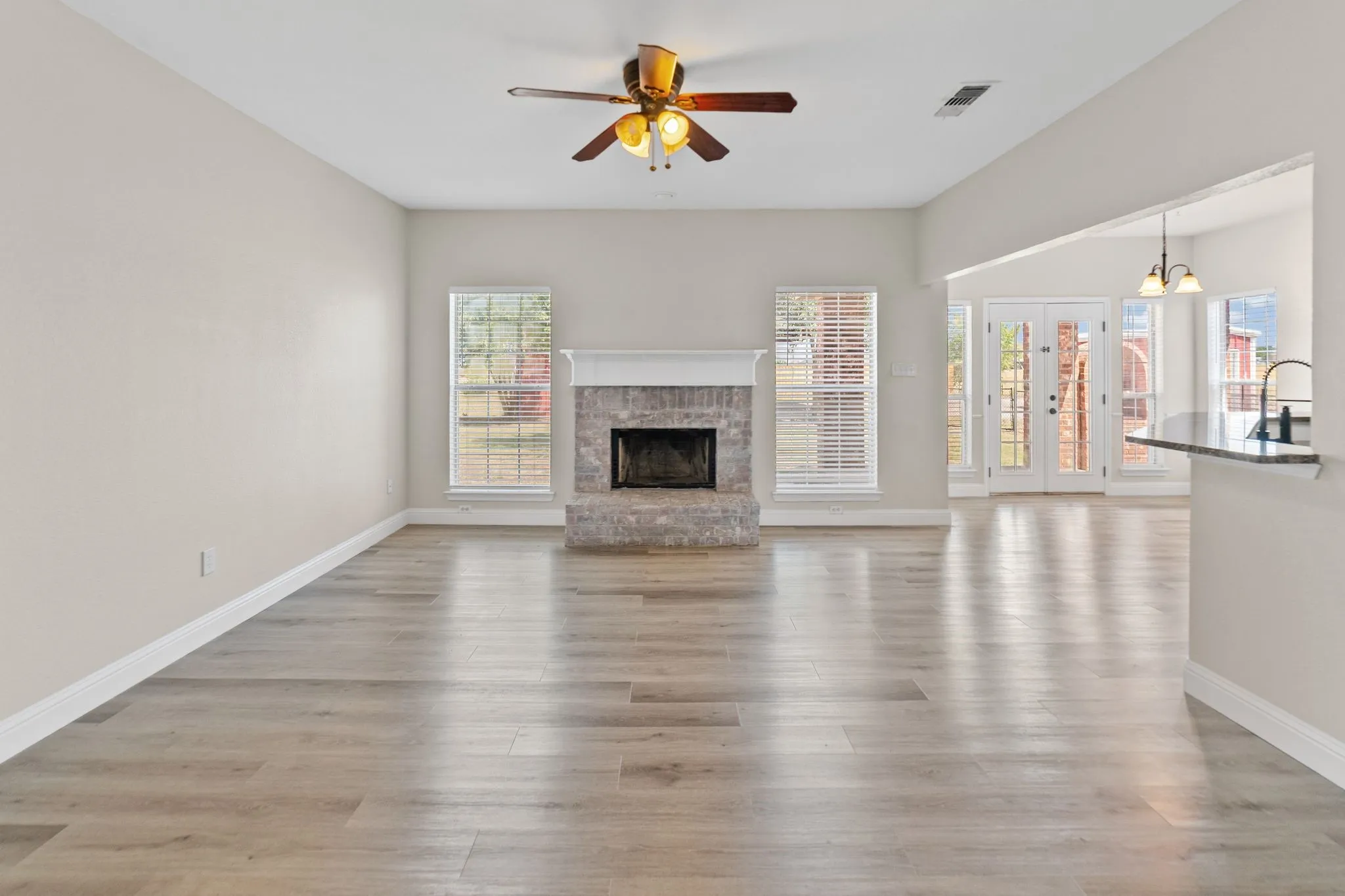 Wood-finish flooring throughout, vaulted ceiling with a ceiling fan, brick fireplace with a mantel, and French doors