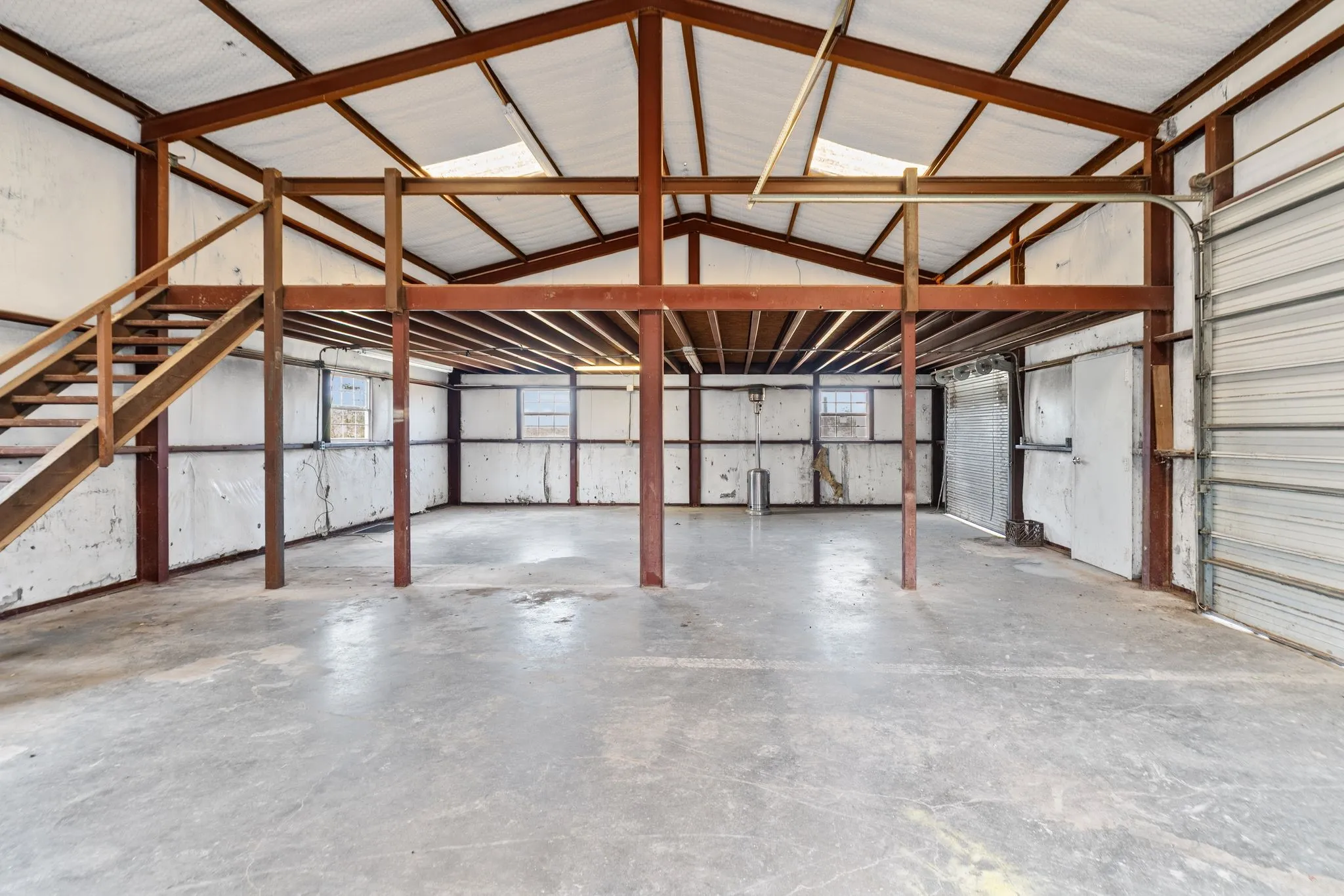 Open-span interior with exposed structural beams, concrete flooring, and an elevated mezzanine with staircase access