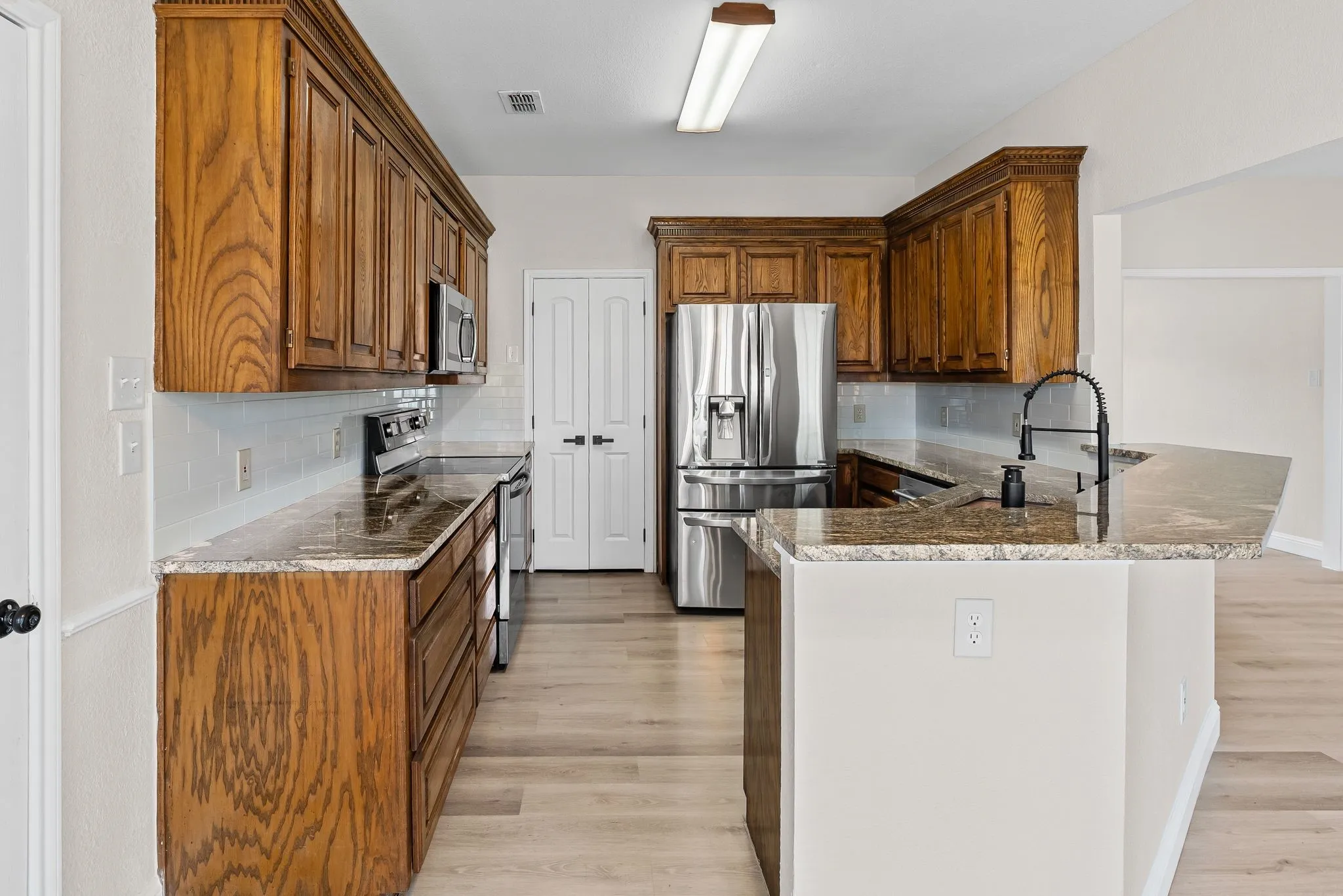 Kitchen featuring wood cabinetry, breakfast bar,  stone countertops, stainless steel appliances, a tile backsplash, and light wood-finish flooring