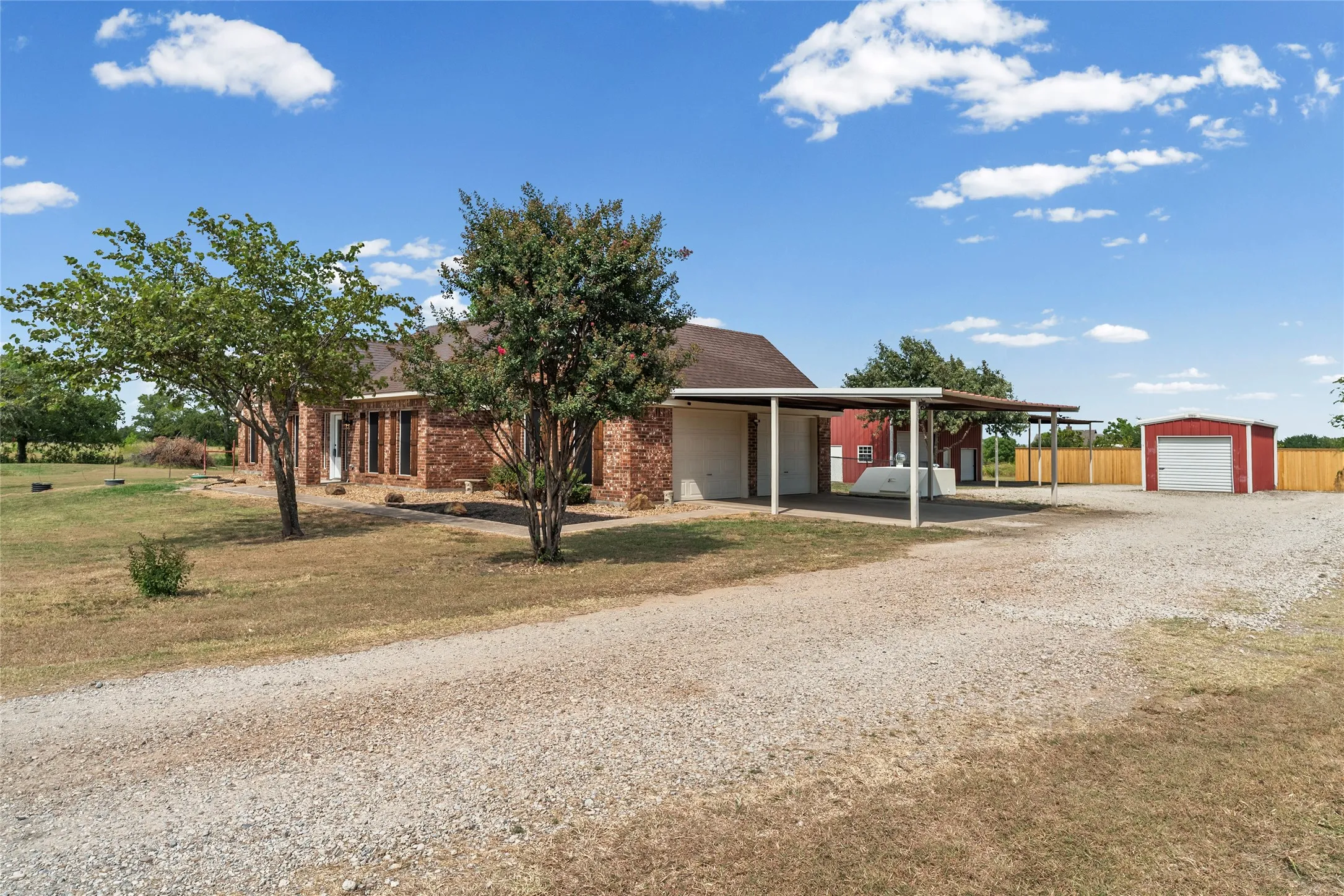 Brick exterior residence with a gravel driveway, covered carport, and a separate red storage building