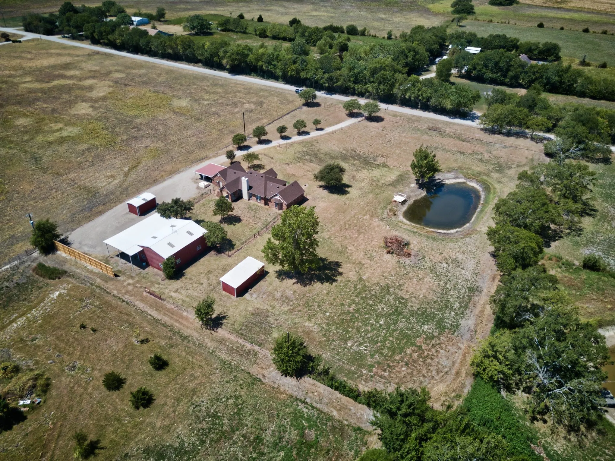Expansive property featuring a single-story residence, multiple outbuildings, a private pond, and mature trees