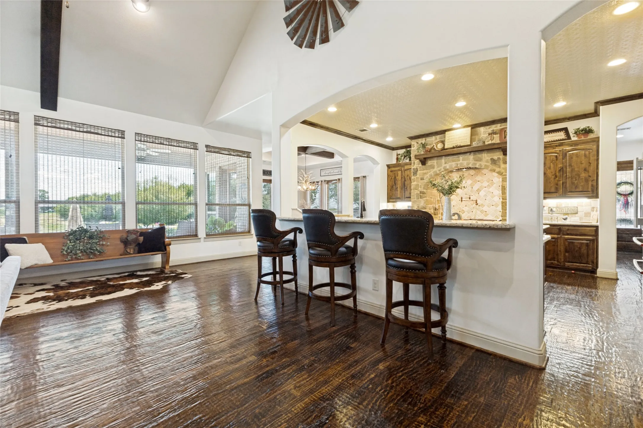 Vaulted ceiling with exposed beam, wood-finish flooring, large windows, kitchen with stone arch, and built-in cabinetry