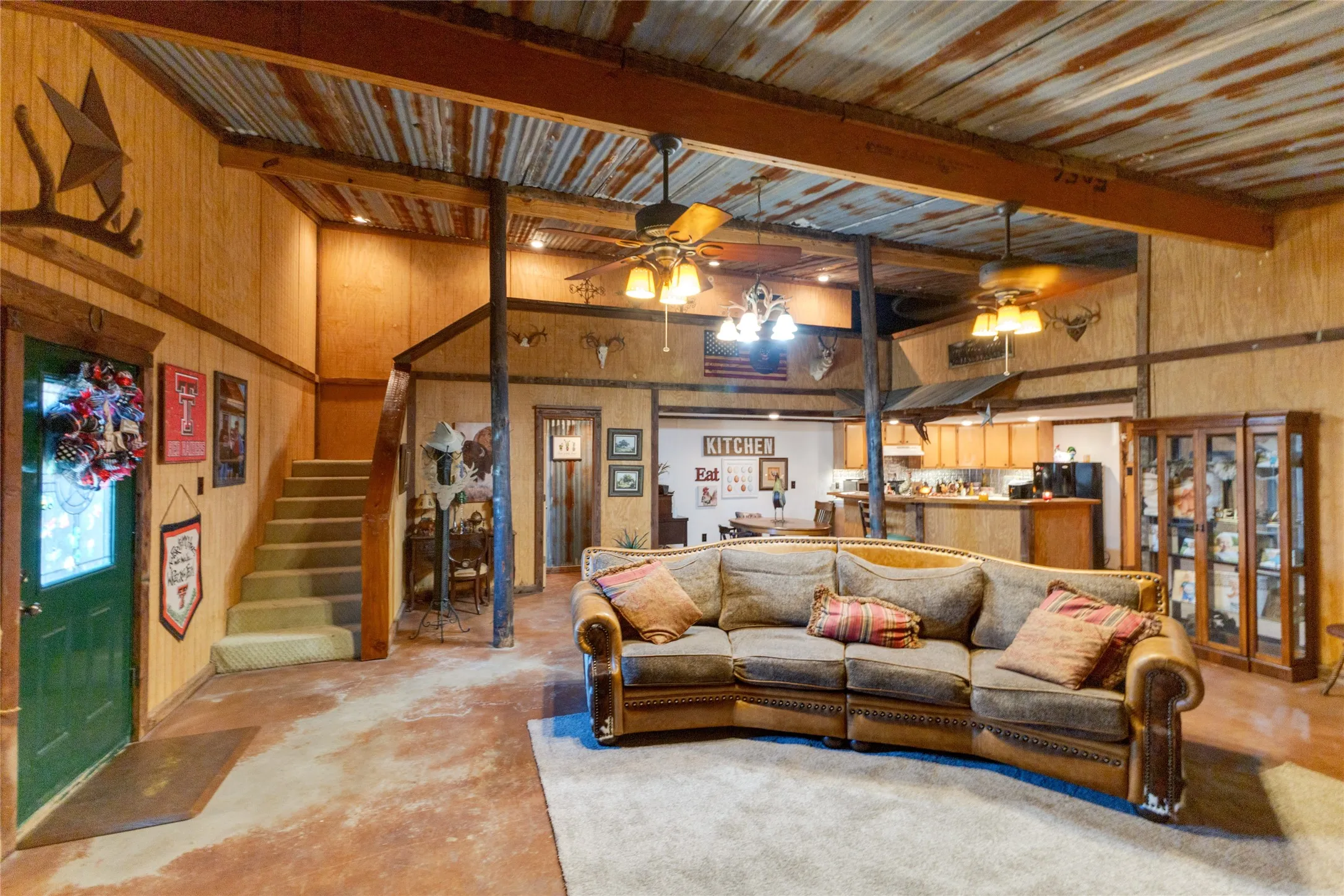 Corrugated metal ceiling panels, exposed ceiling beams, wood-paneled walls, stained concrete flooring, and a built-in display cabinet
