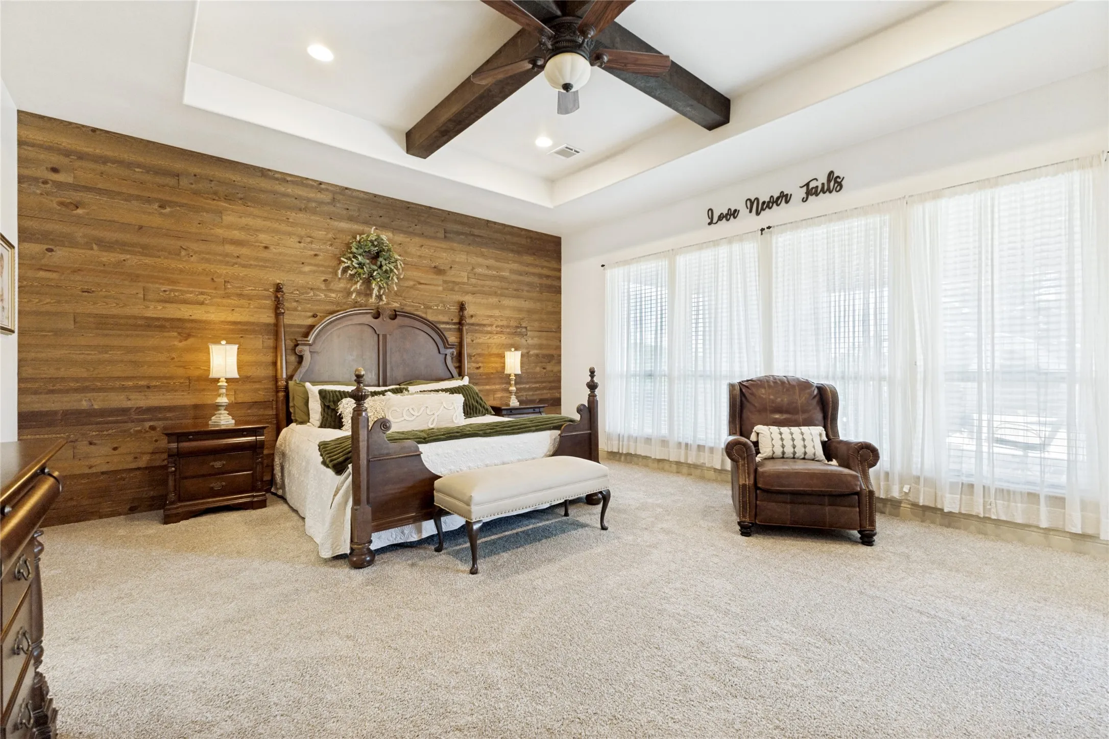 Wood-paneled accent wall, tray ceiling, recessed lighting, and multiple windows