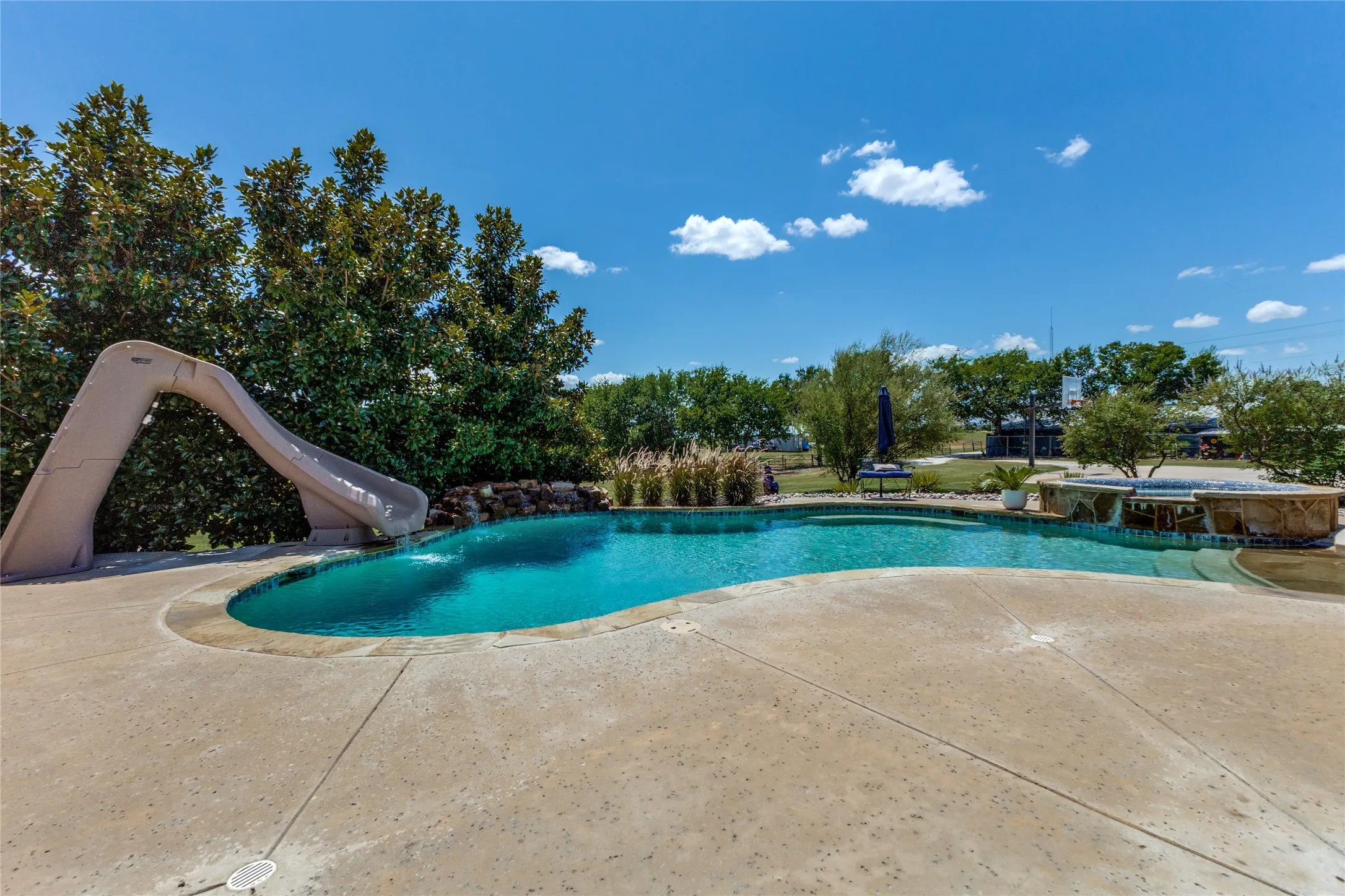 Lagoon-style pool featuring a water slide, integrated spa, and rock waterfall