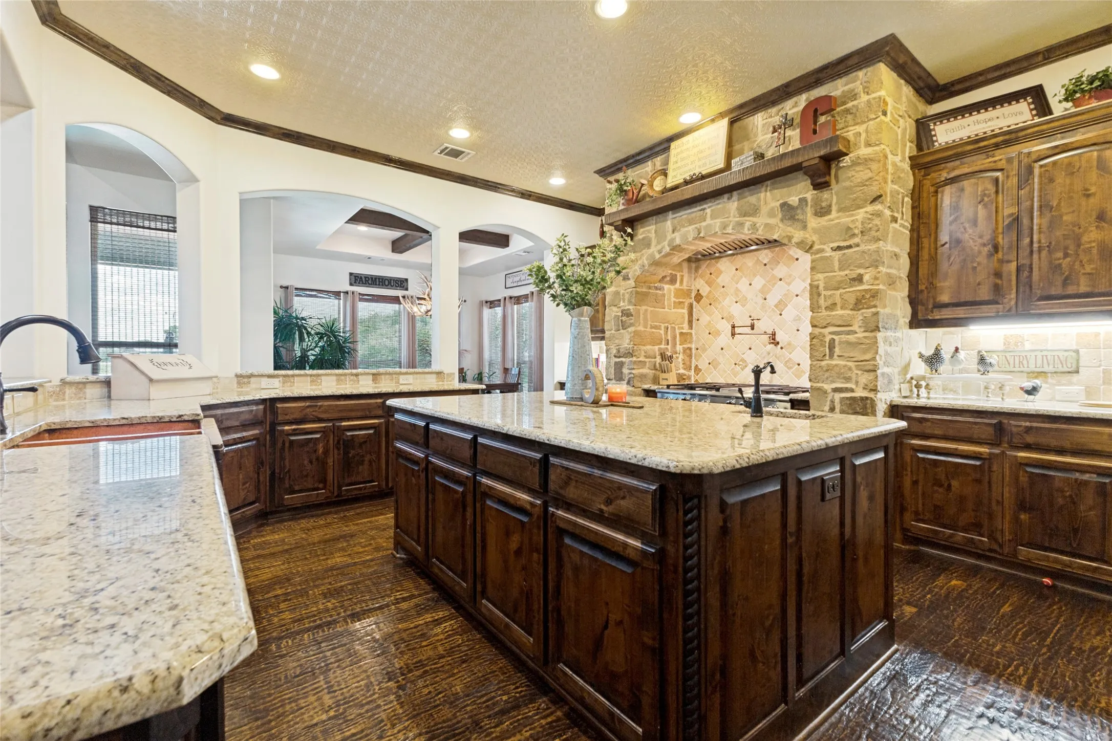 Central island with integrated storage, stone countertops, dark wood cabinetry, a stone-clad range hood, and wood-finish flooring