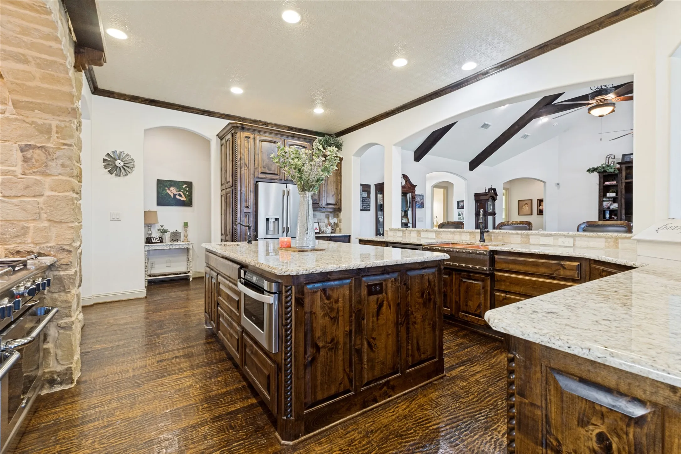 Kitchen featuring wood-finish flooring, granite countertops, custom wood cabinetry, a built-in stainless steel microwave, and exposed ceiling beams