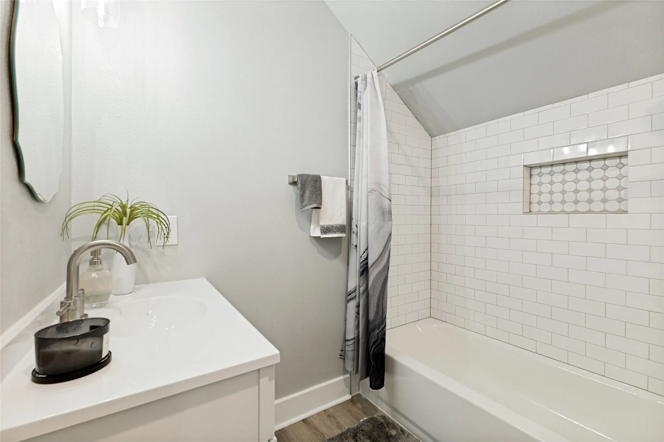 Contemporary bathroom featuring a single vanity with a white countertop and undermount sink, a brushed nickel faucet, subway tile bath surround, and a recessed shower niche with decorative tile