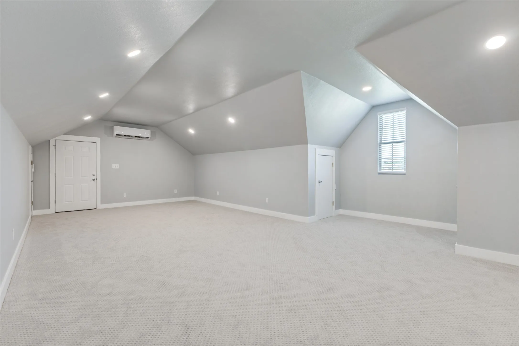 Spacious room featuring sloped ceilings, recessed lighting, carpet flooring, a window with blinds, and built-in climate control