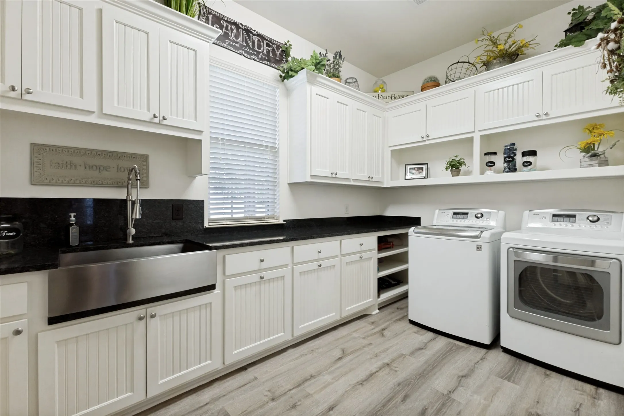 Expansive utility room featuring wood-finish flooring, white cabinetry, black countertops, and a stainless steel farmhouse sink