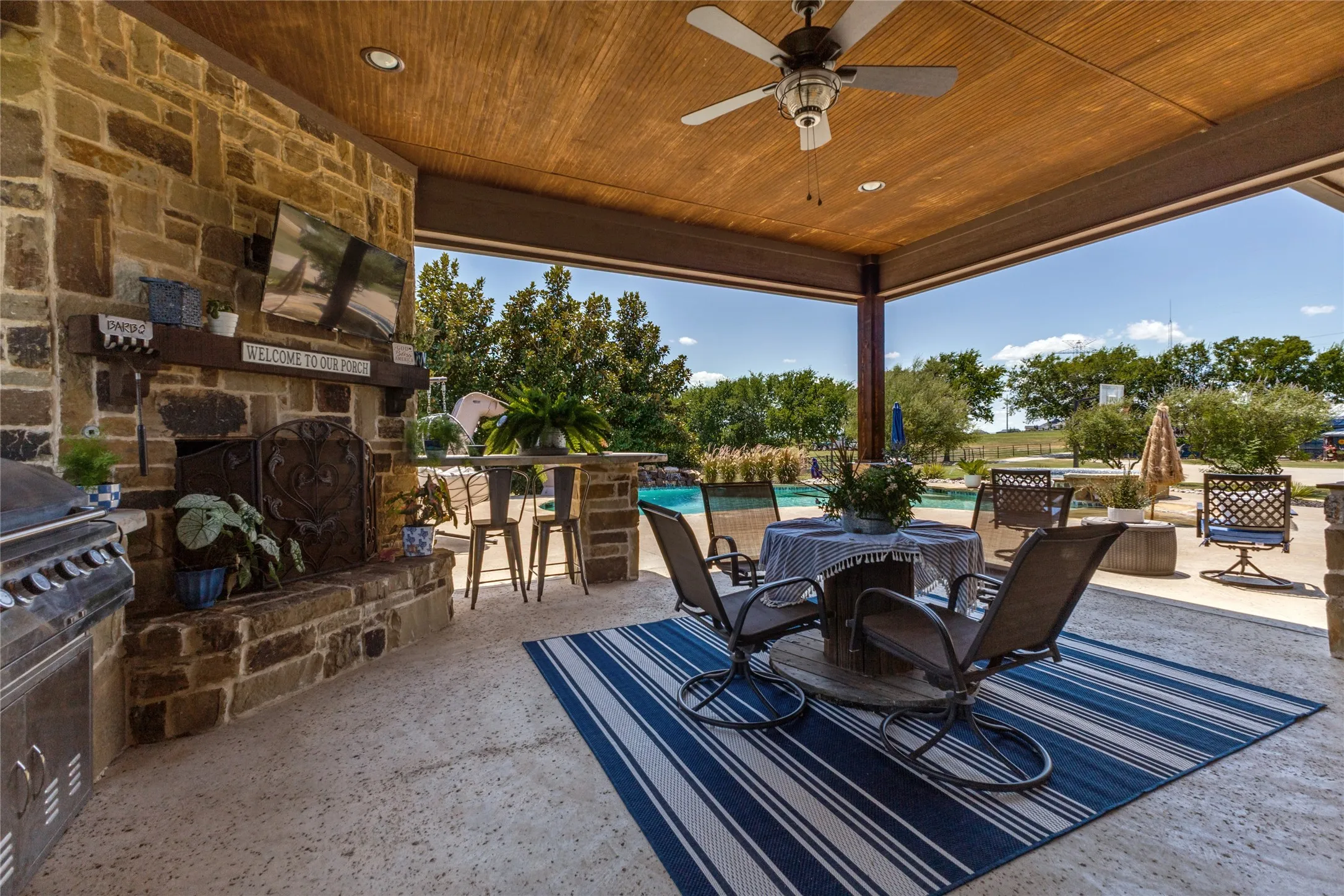 Outdoor living area with stone fireplace, built-in grill station, ceiling fan, and wood-paneled ceiling