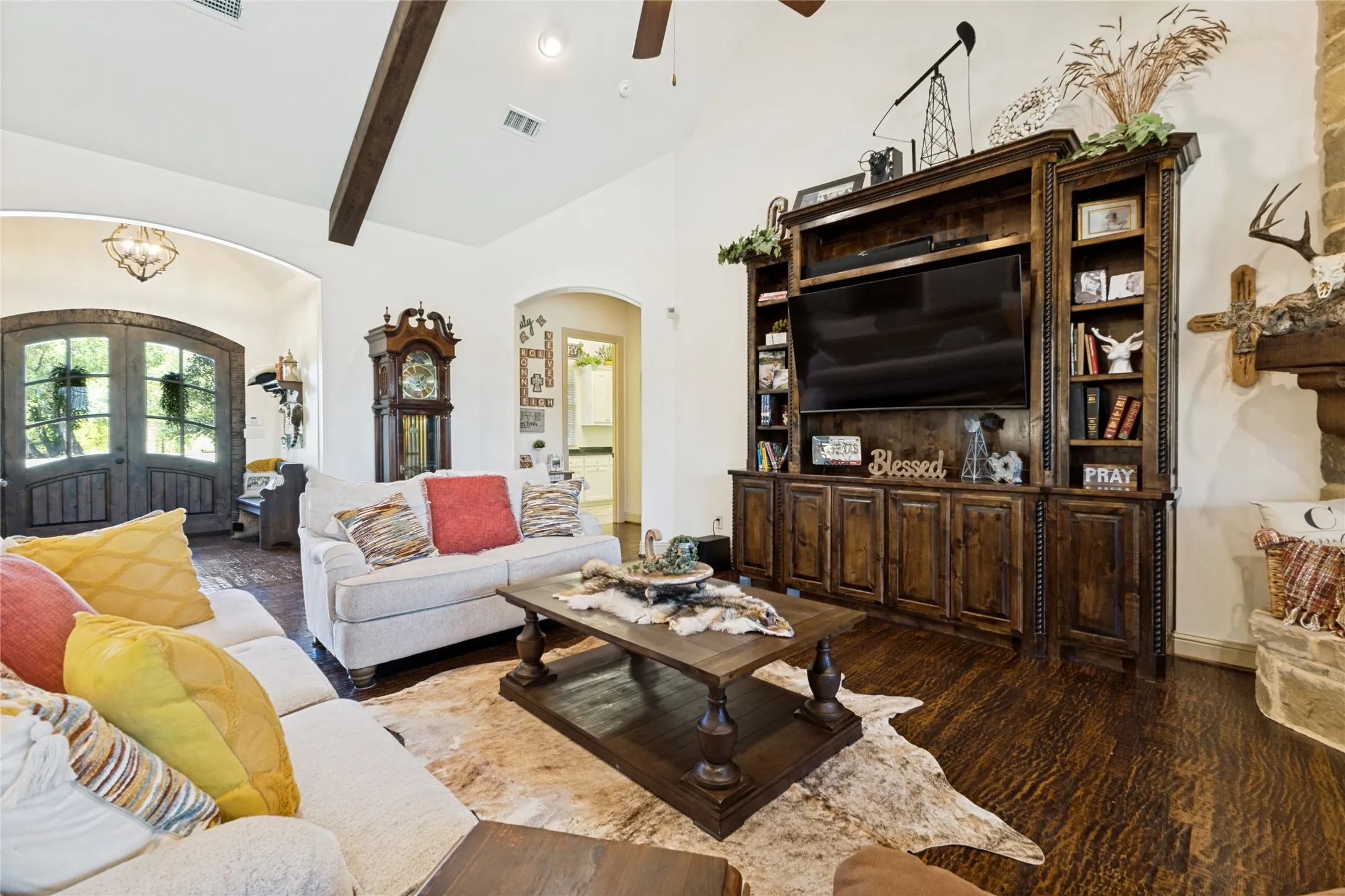Vaulted ceilings with exposed wood beams, dark wood-finish flooring, built-in entertainment center with shelving and storage, archway entry, and double entry doors