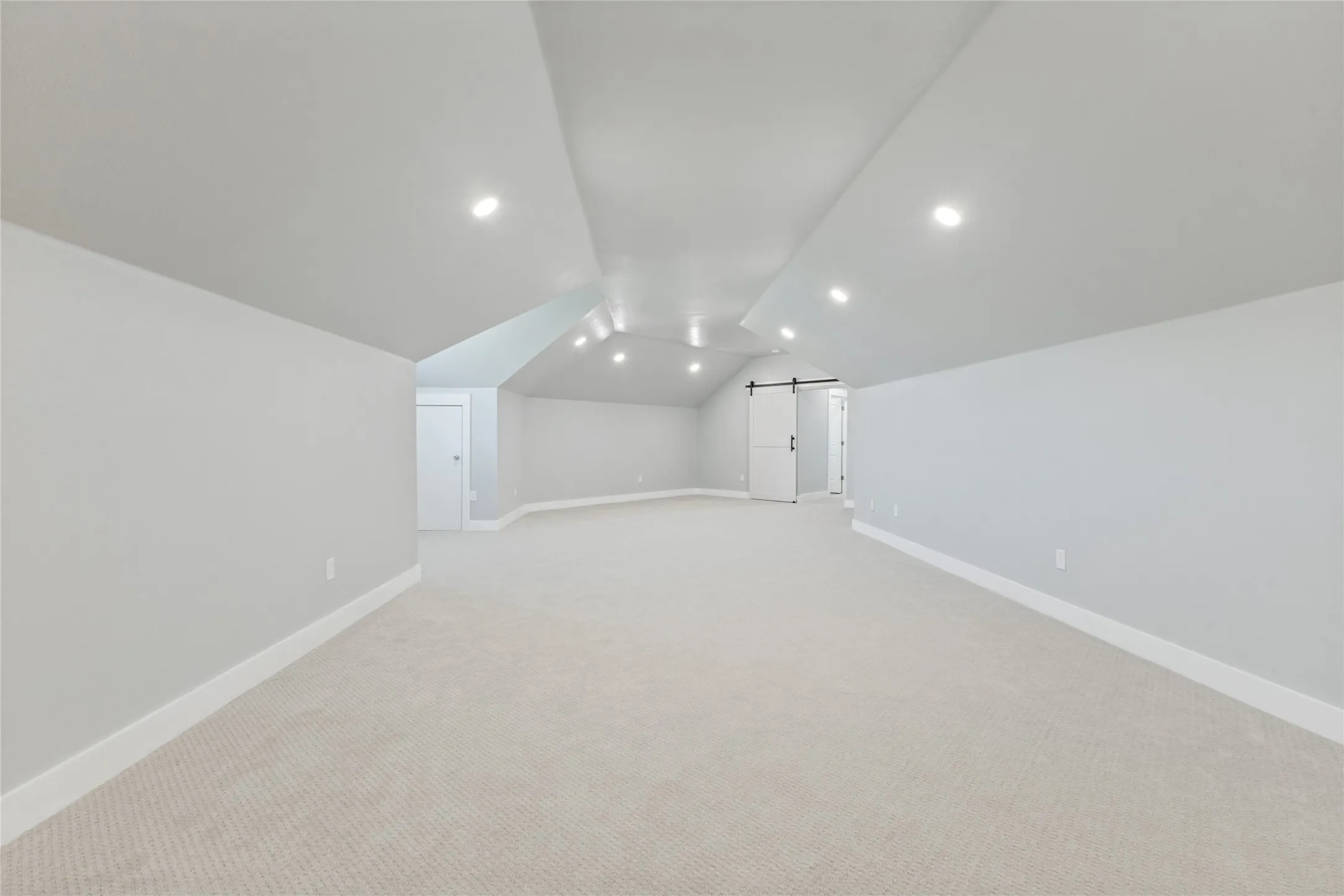 Spacious room featuring vaulted ceilings, recessed lighting, neutral wall finishes, carpeted flooring, and a barn door