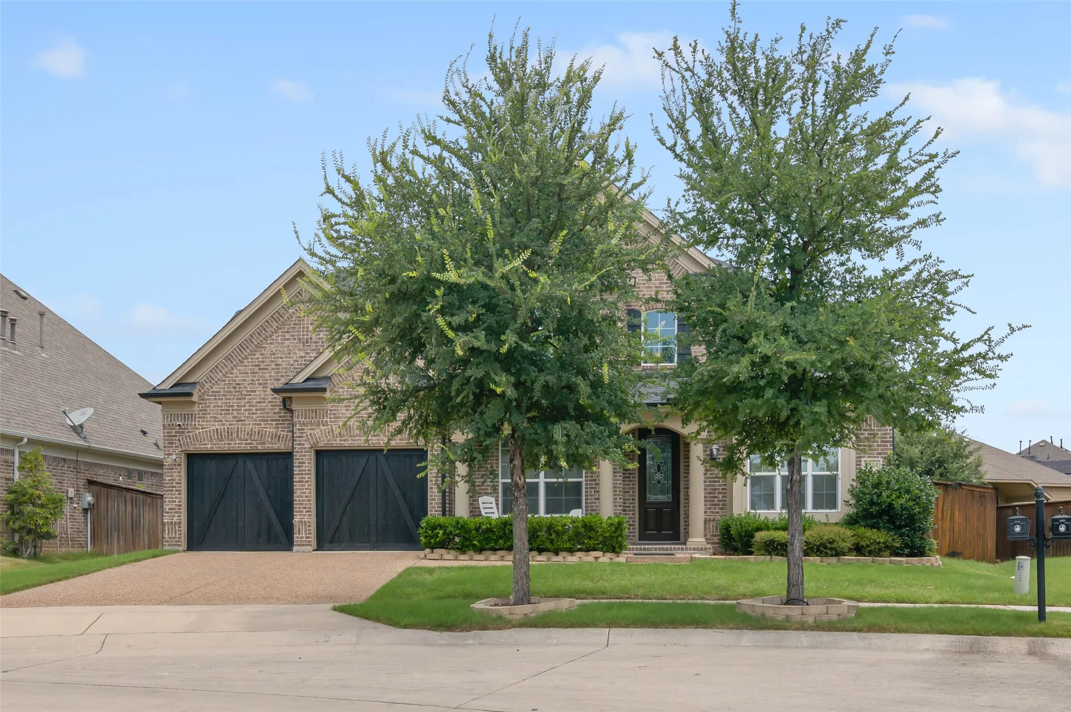 Brick exterior with stone accents, mature trees, two-car garage with dark wood doors, and a covered entry