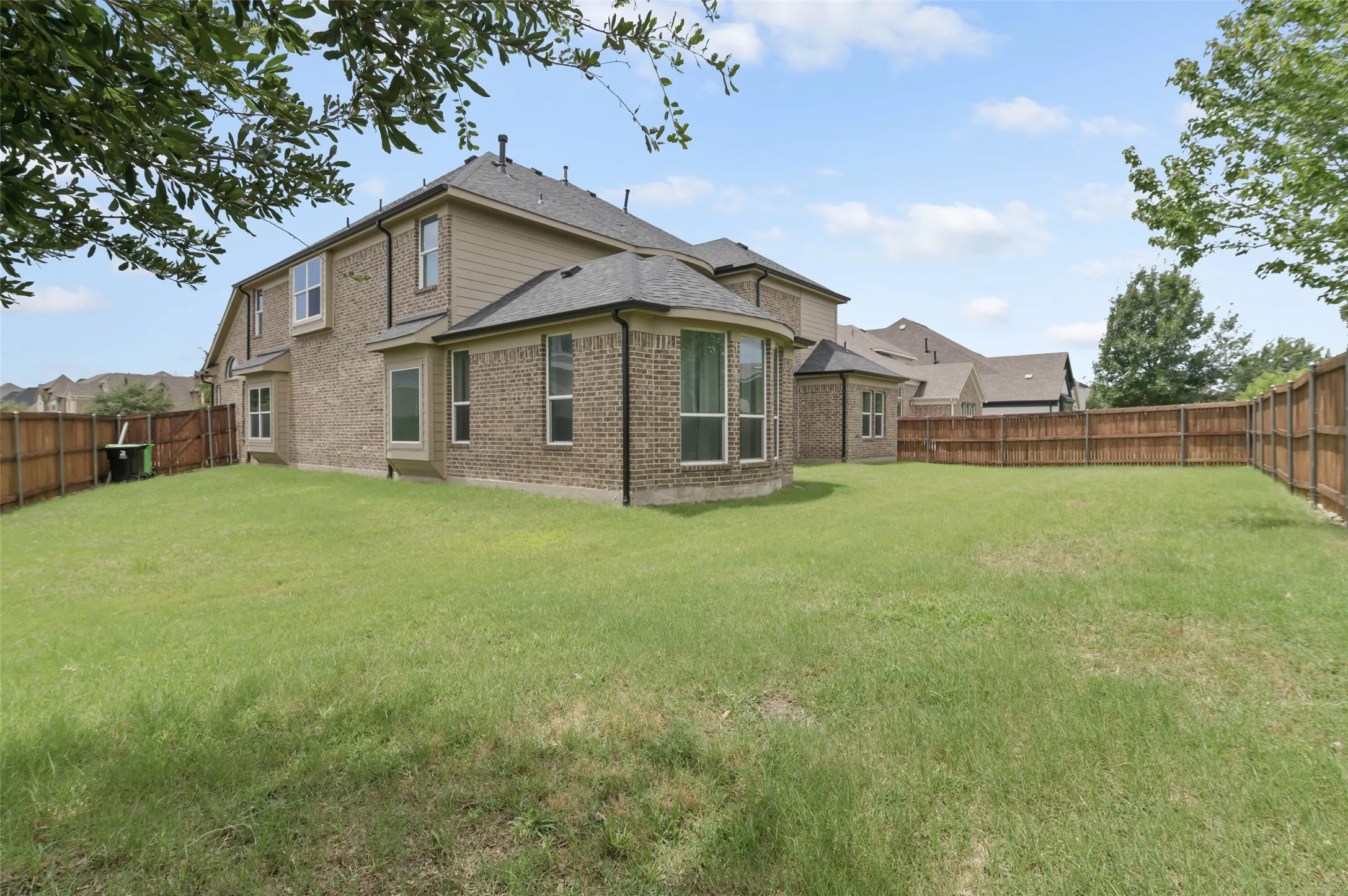Expansive backyard featuring a manicured lawn, wood fencing, and a multi-level brick and siding exterior