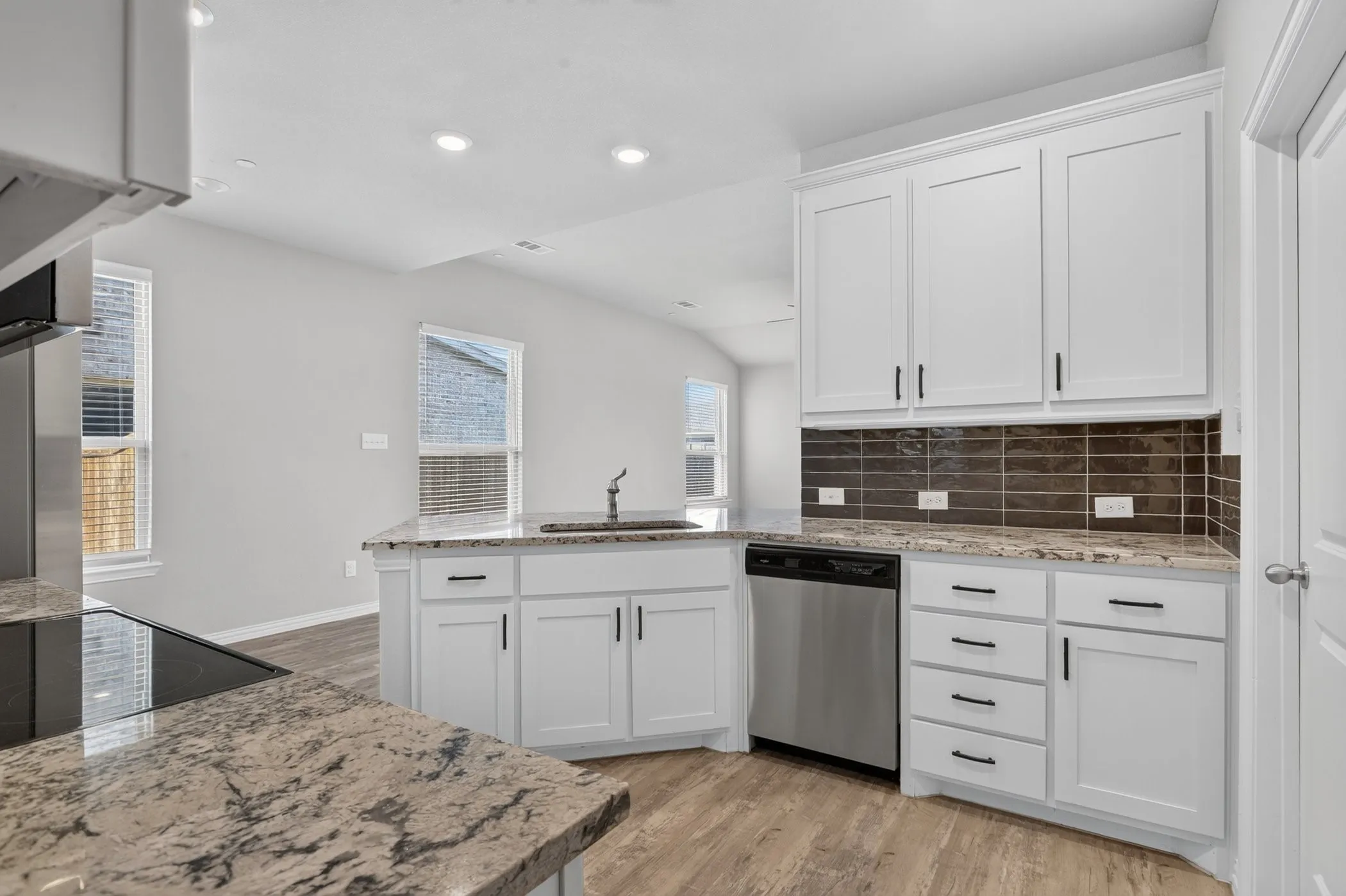 Kitchen featuring white cabinetry, stone countertops, a tile backsplash, stainless steel appliances, and wood-finish flooring