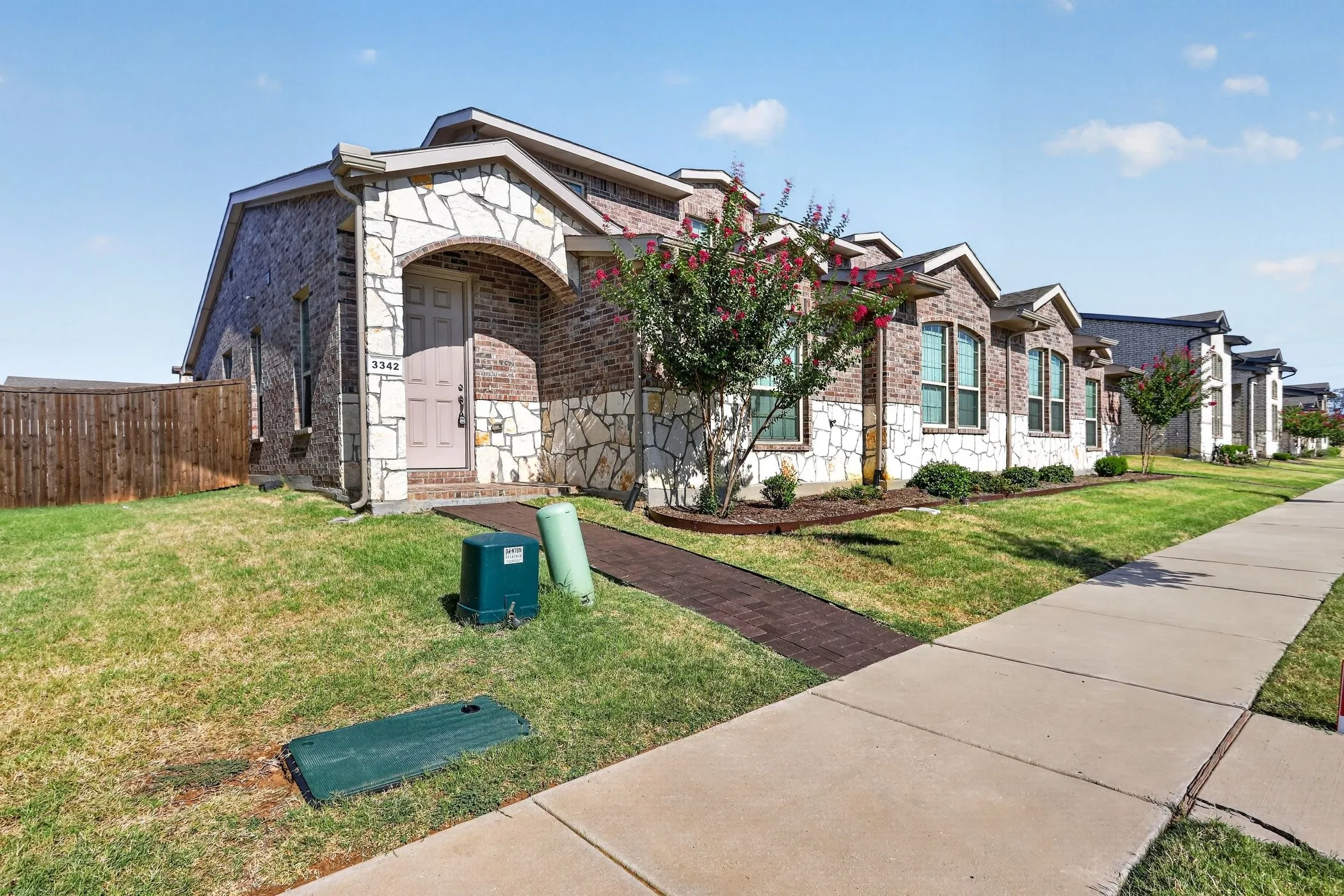 Brick and stone exterior with arched entryway, concrete walkway, and established landscaping