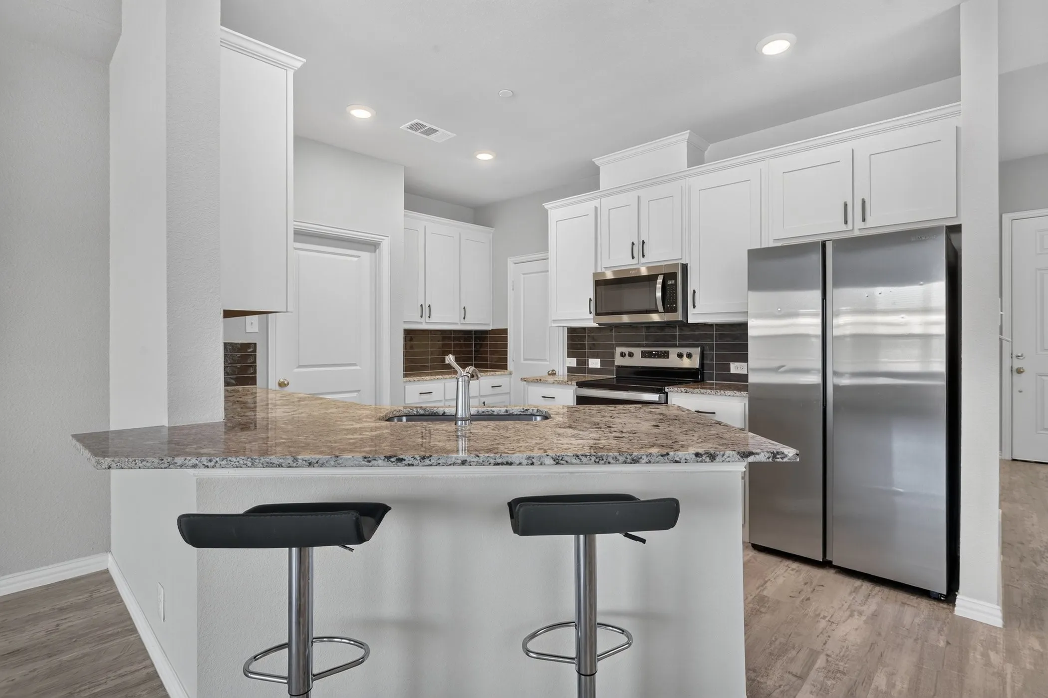Kitchen featuring white cabinetry, stainless steel appliances, granite countertops, a built-in breakfast bar, and wood-finish flooring