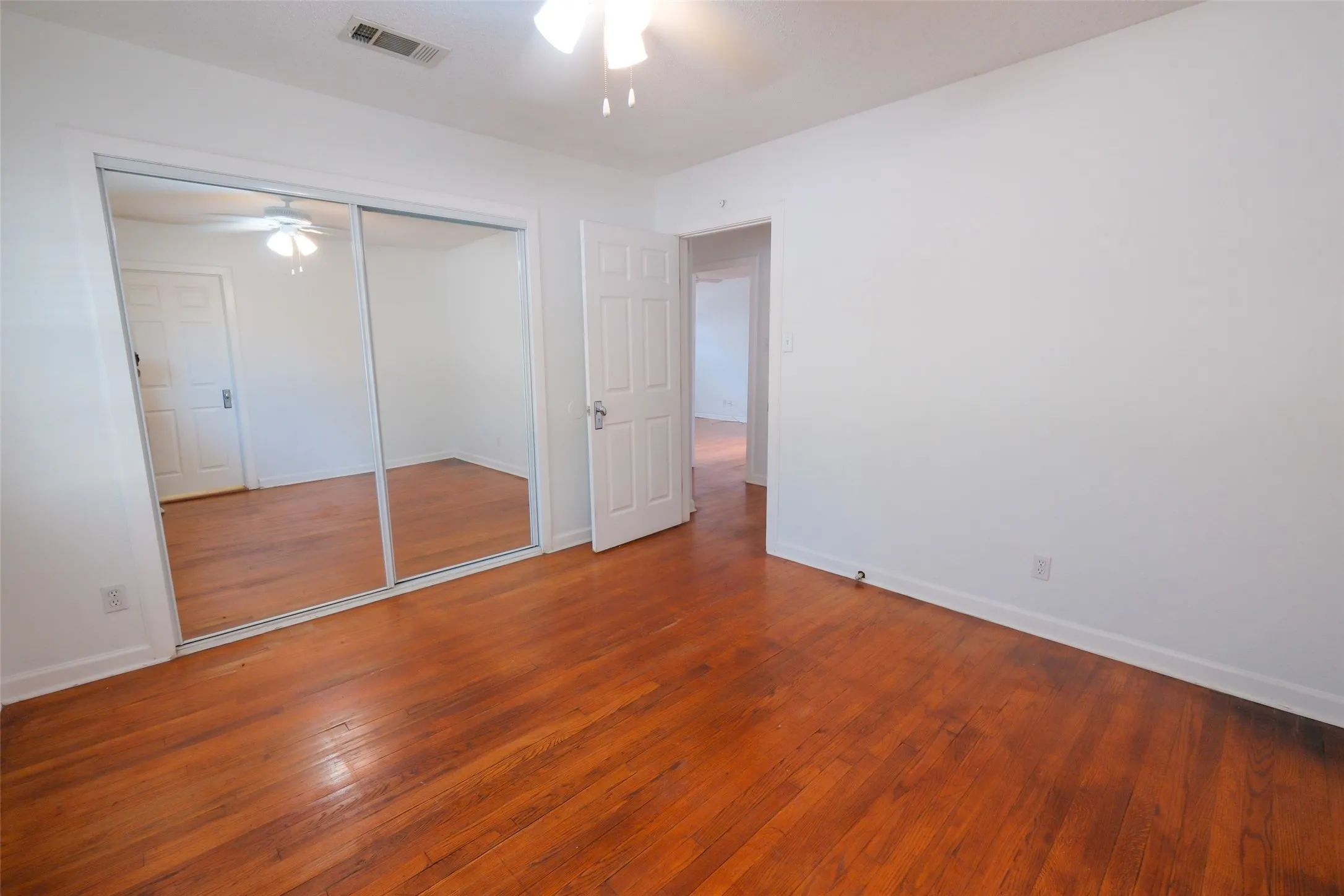 Hardwood flooring throughout, mirrored closet doors, and a ceiling fan