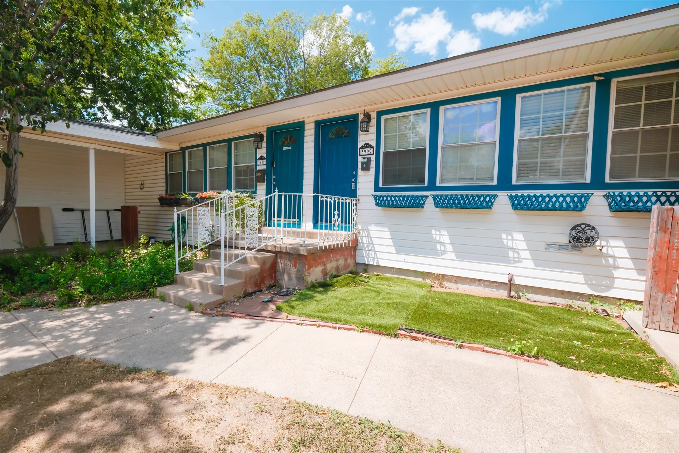 White siding exterior with teal trim, dual teal entry doors, front porch with white railings, and artificial turf landscaping