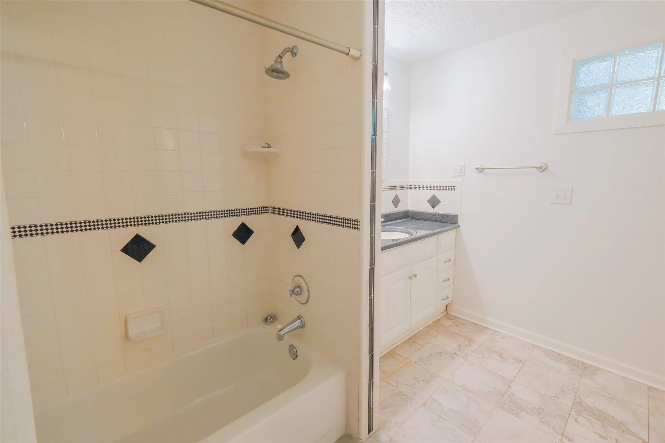 Tub and shower combination featuring tiled surround, single vanity with integrated sink, glass block window, and tiled flooring