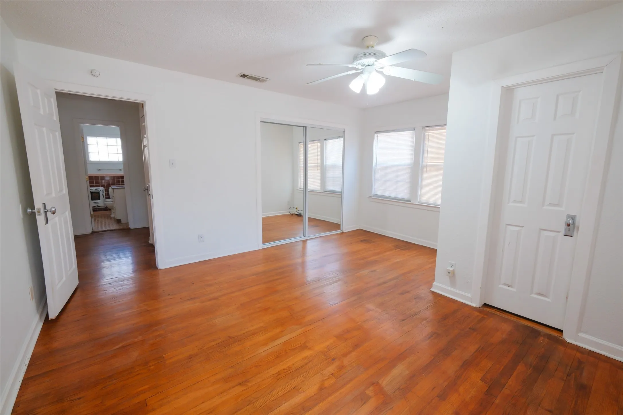 Wood-finish flooring throughout, white paneled doors, and a ceiling fan with integrated lighting