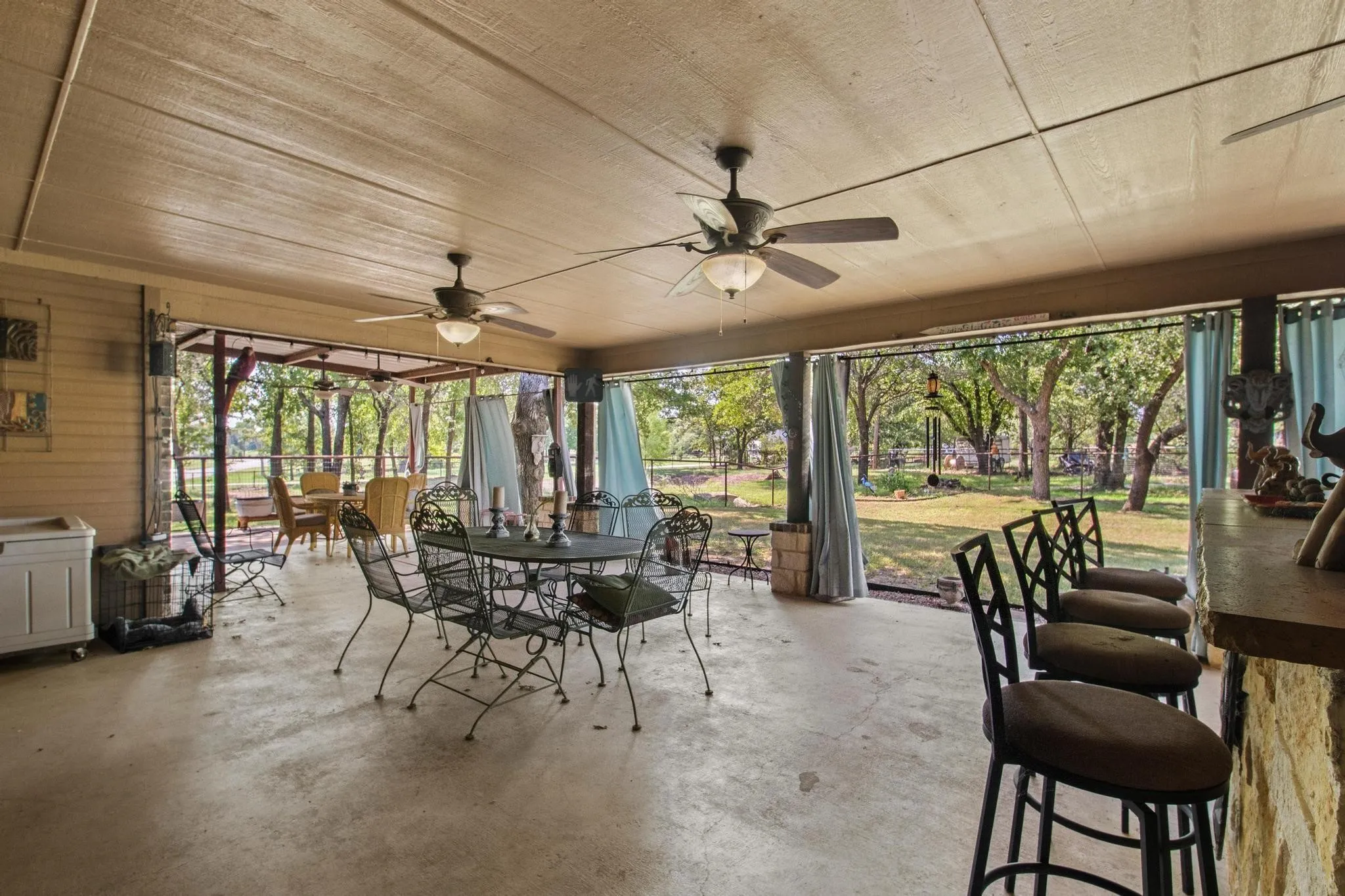 Expansive covered patio featuring multiple ceiling fans, exposed beam ceiling, stone-faced bar, and a screened enclosure offering outdoor living