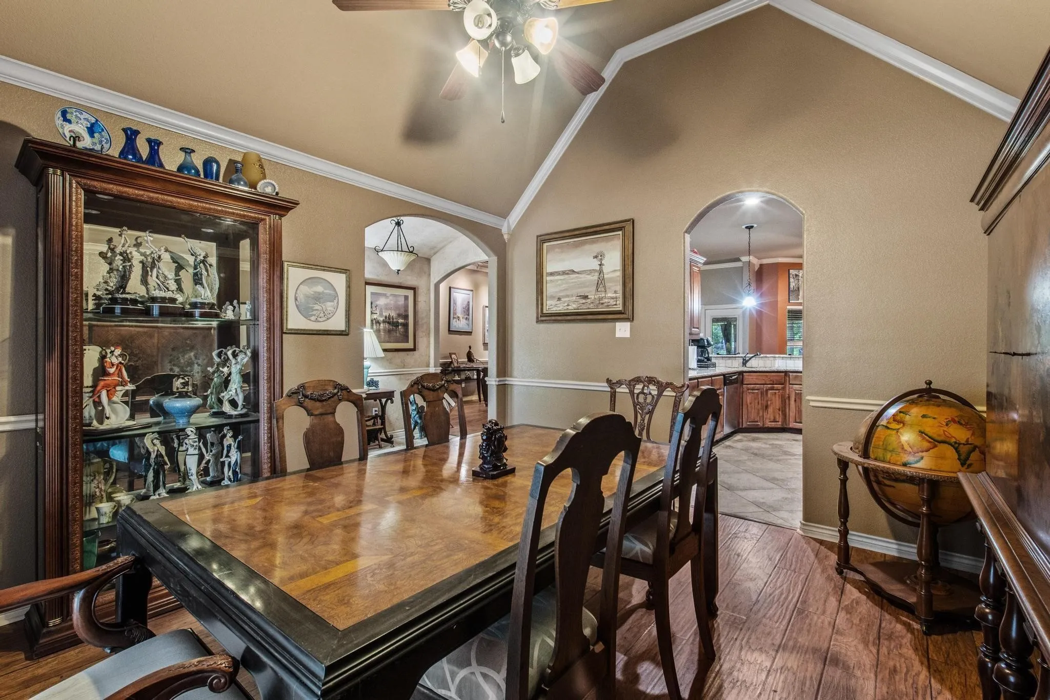 Vaulted ceiling with a ceiling fan, crown molding, wood-finish flooring, and arched doorways