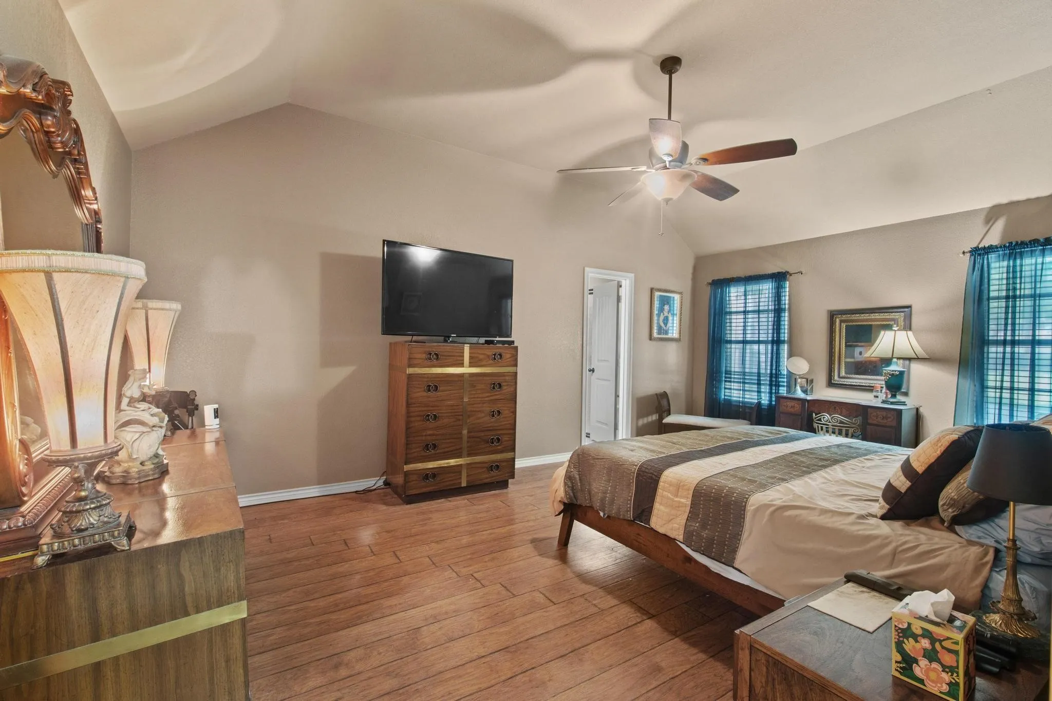 Vaulted ceiling with a ceiling fan, wood-finish flooring, and two windows