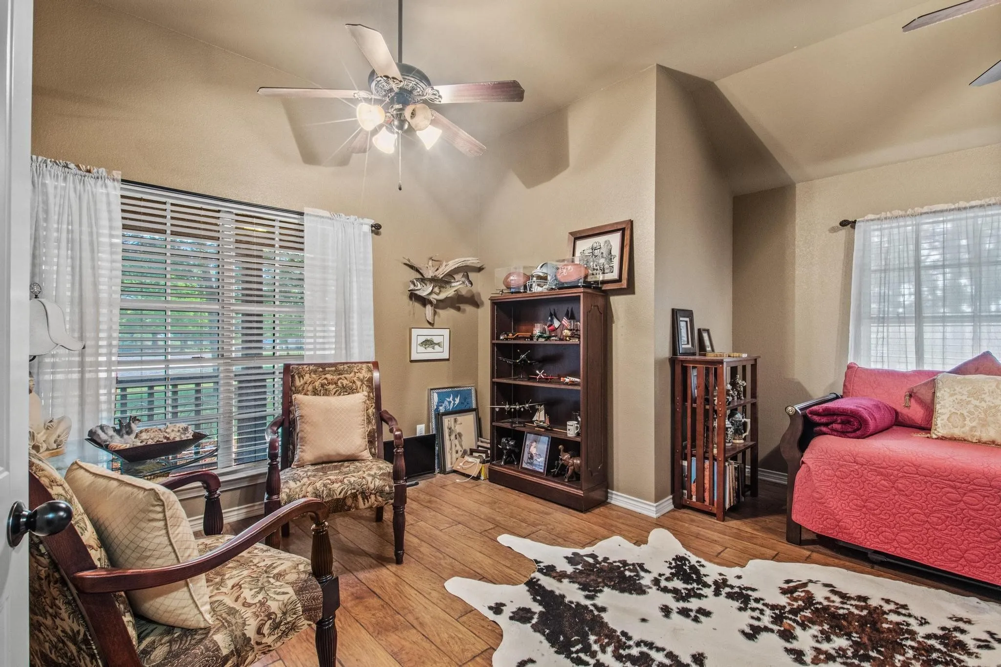 Vaulted ceiling with ceiling fan, large window with blinds, wood-finish flooring, and built-in shelving