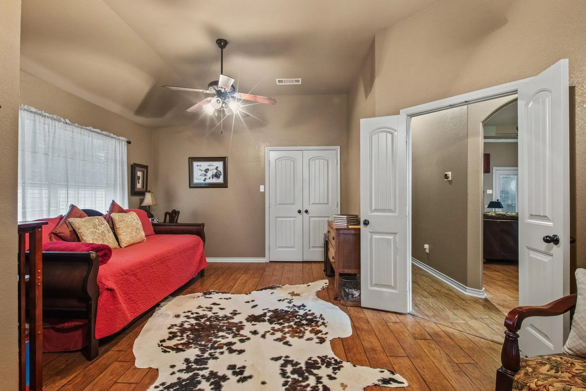 Tray ceiling, wood-finish flooring, ceiling fan with integrated lighting, white panel doors, and an arched doorway