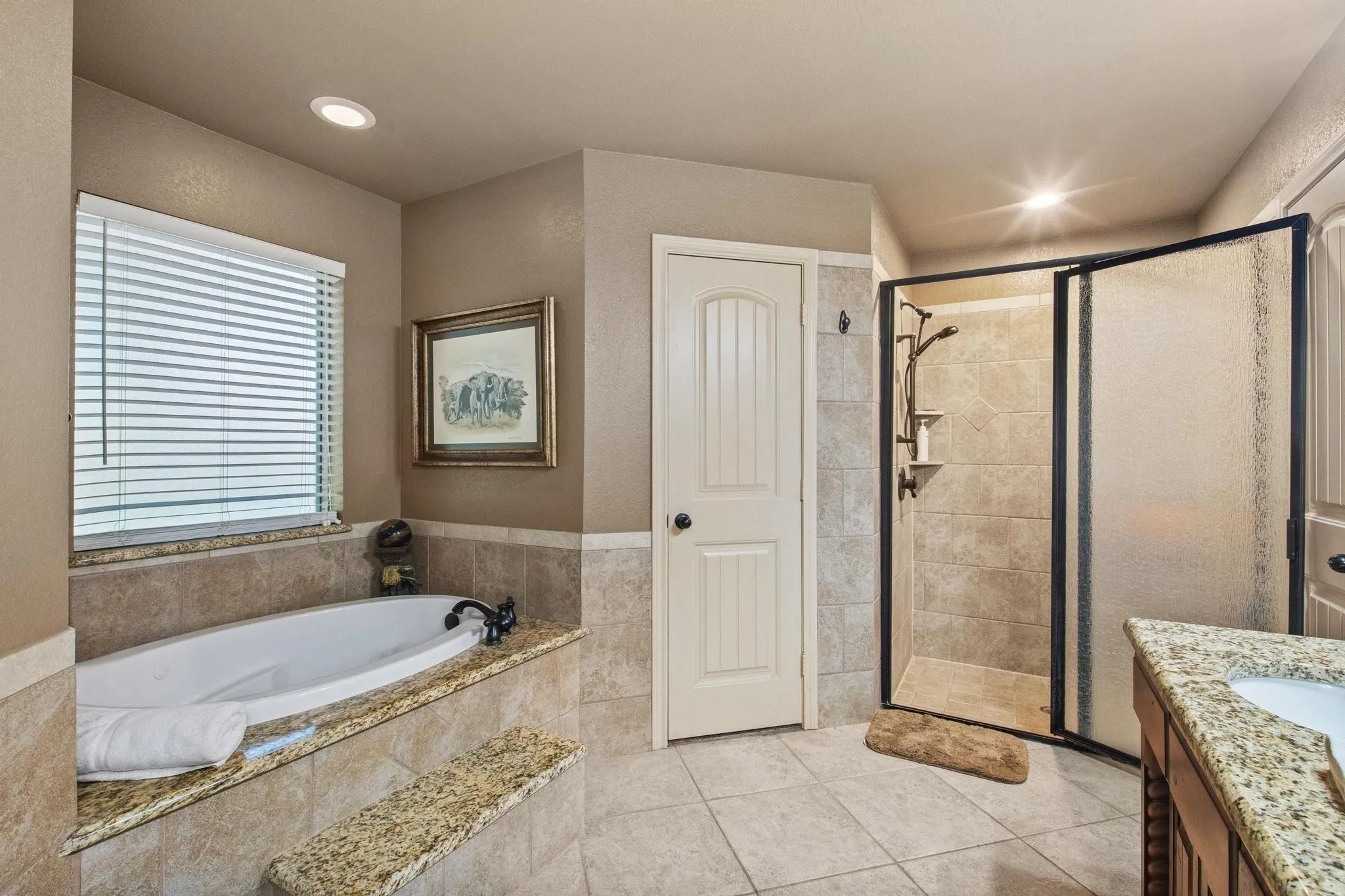 Recessed lighting illuminates a built-in soaking tub with a tiled surround and an adjacent shower with a framed glass enclosure