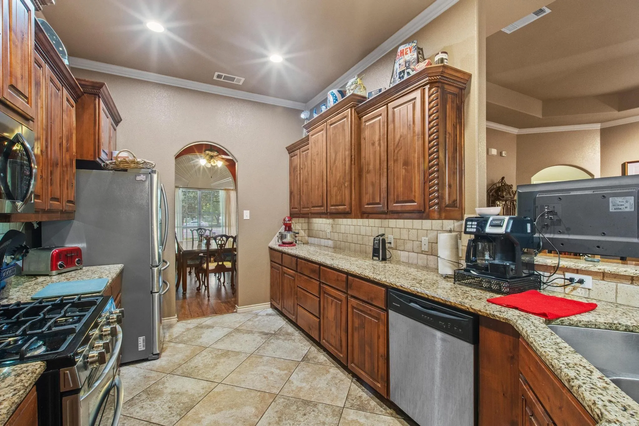 Kitchen featuring wood cabinetry, granite countertops, tile flooring, stainless steel appliances, and recessed lighting