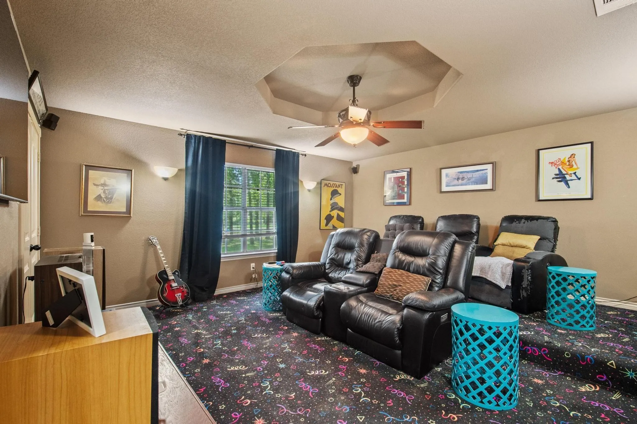 Room featuring an octagonal tray ceiling, ceiling fan, wall-mounted sconces, and a large window with privacy drapes
