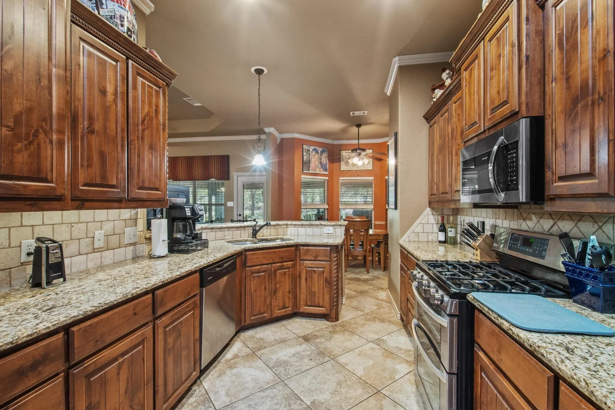 Wood cabinetry with crown molding, granite countertops, tile backsplash, stainless steel appliances, and tile flooring