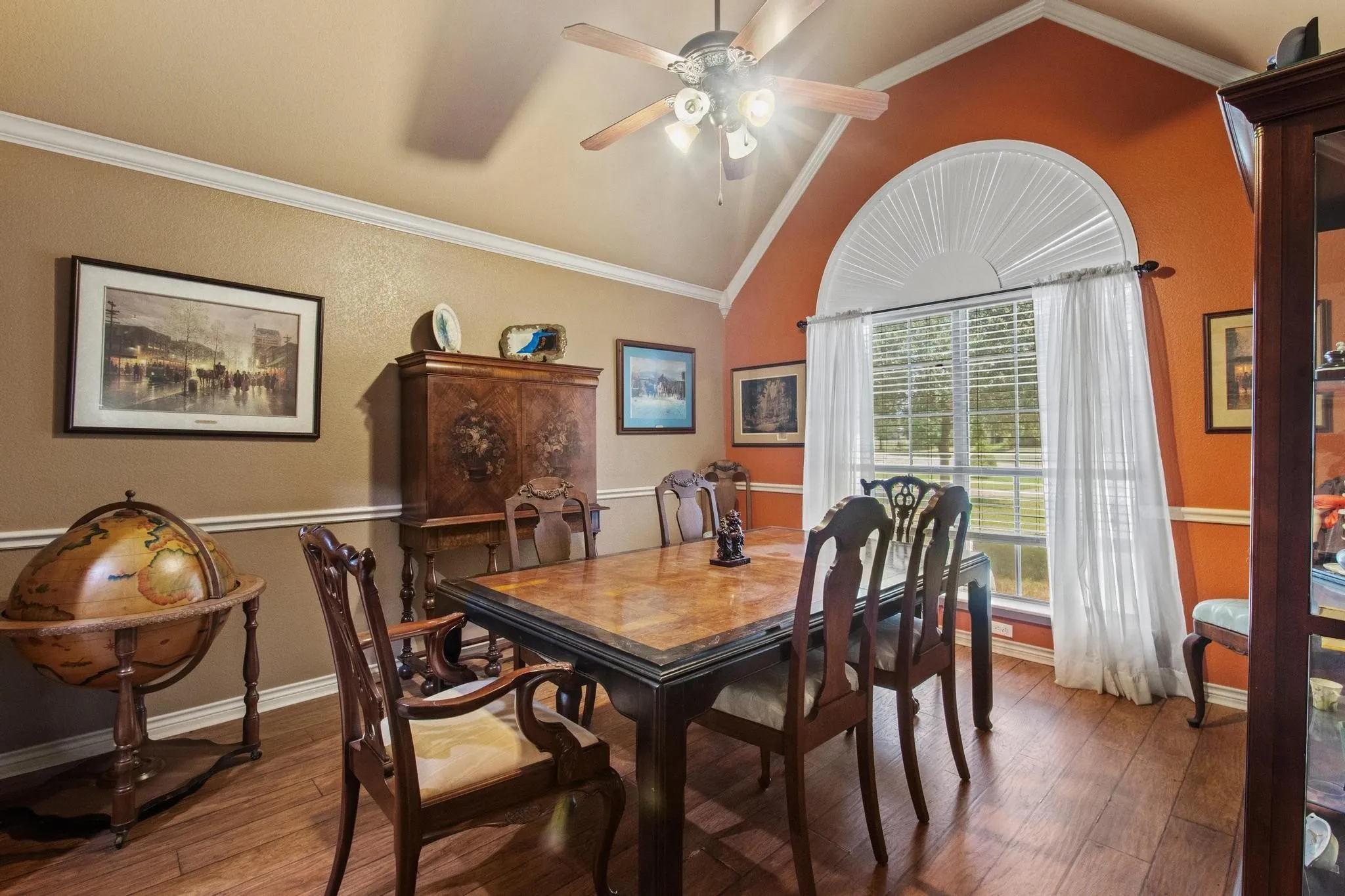 Wood-finish flooring, vaulted ceiling, crown molding, wall paneling, and an arched window with a sunburst detail