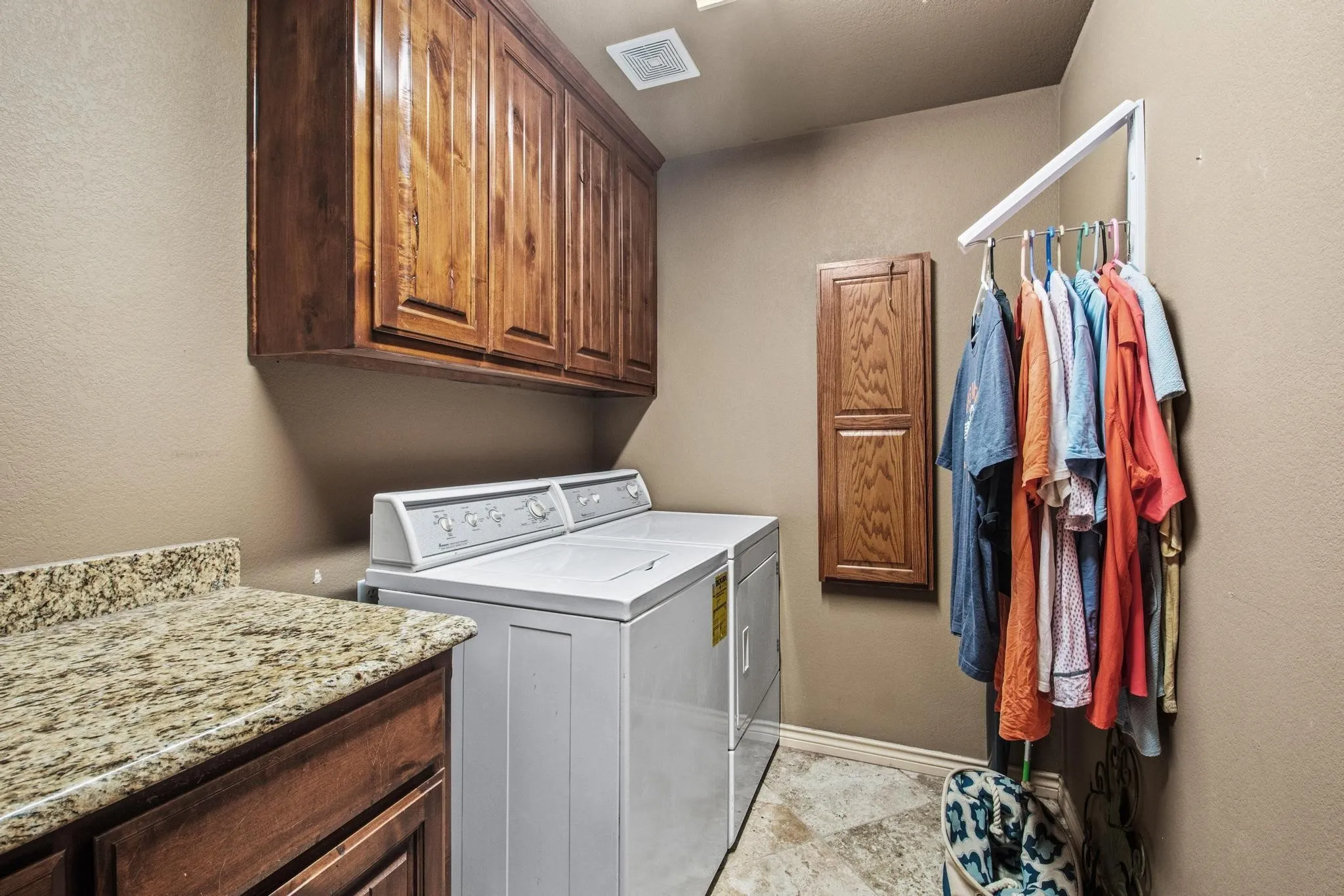 Laundry area featuring wood cabinetry, stone-finish countertop, and tile flooring